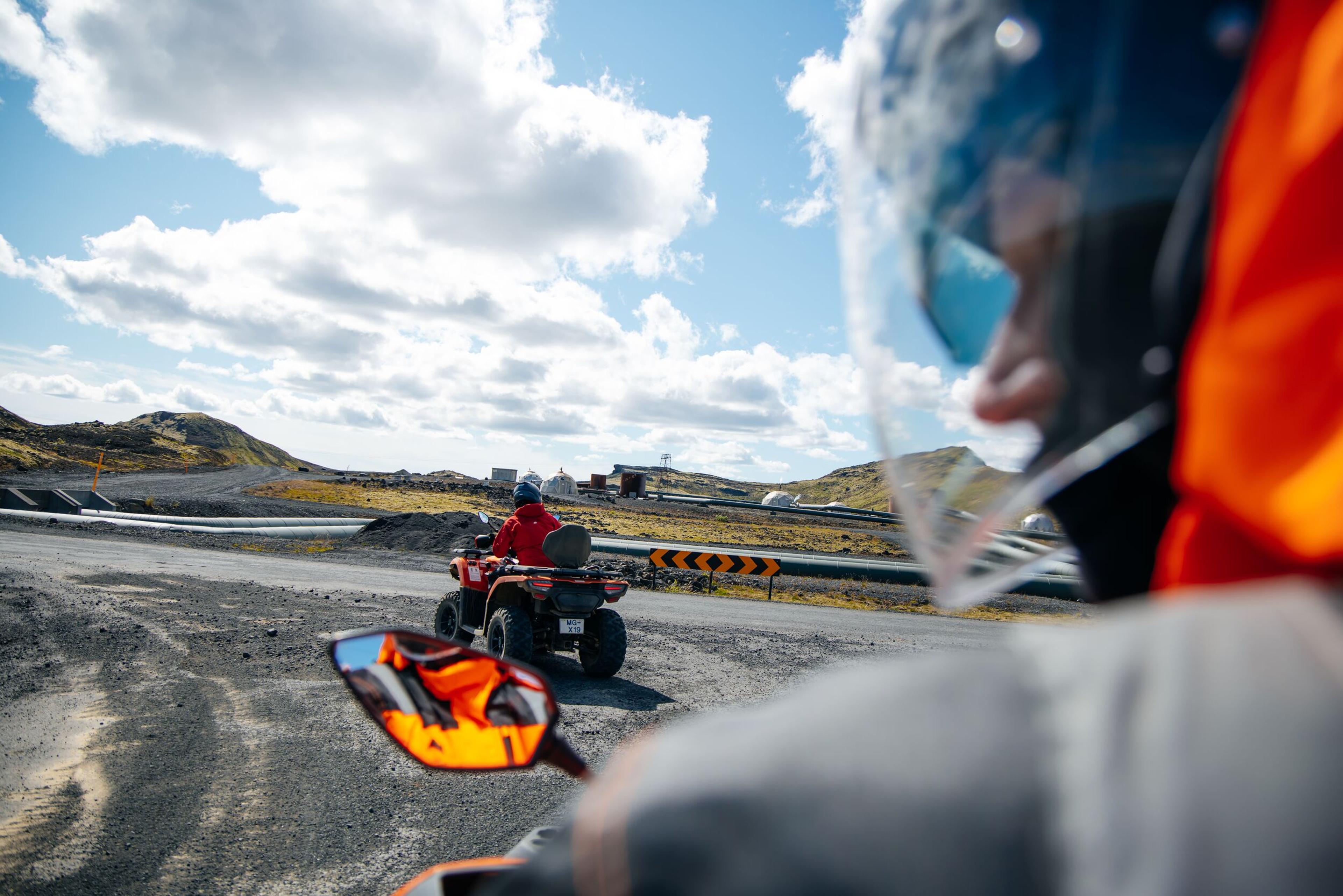 Helmeted rider's view of another ATV on a gravel road in a rugged landscape.