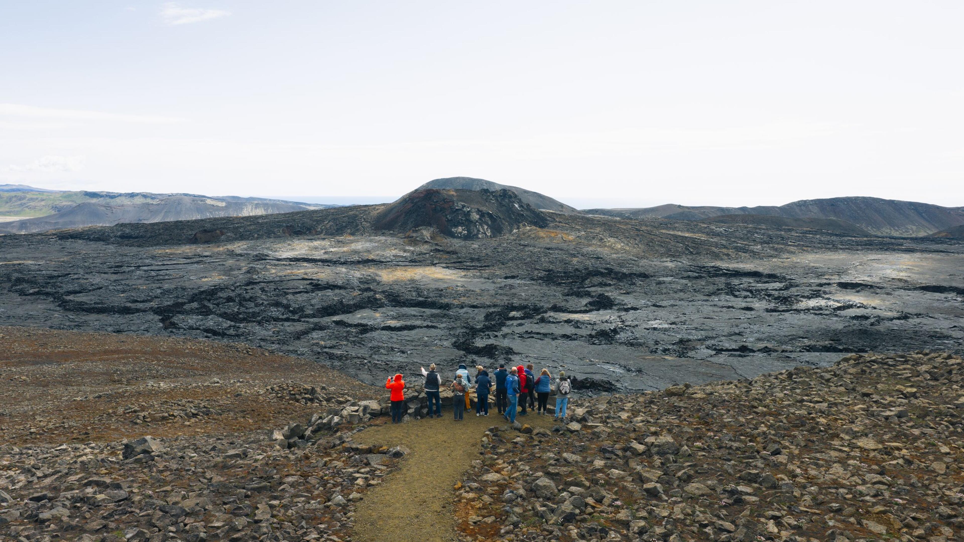 a group of people are standing on top of a rocky hill looking at a volcano .