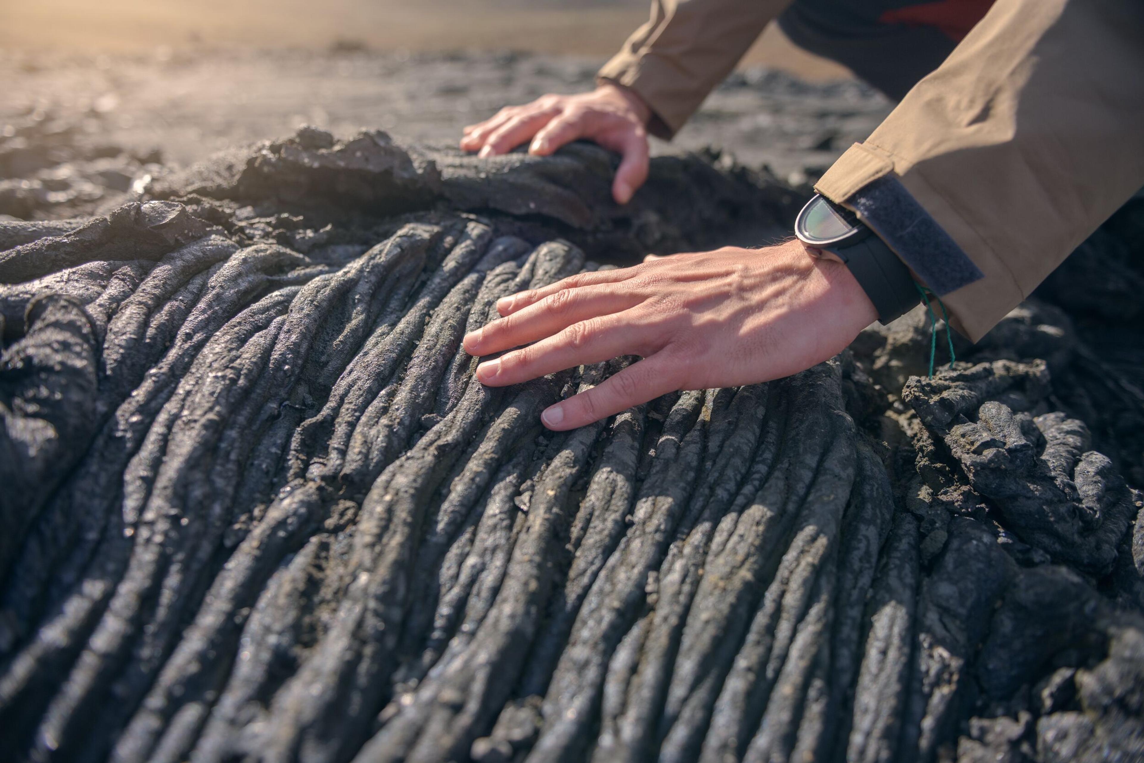 A hand gently touching the intricately patterned surface of freshly solidified lava, revealing its mesmerizing and captivating textures.