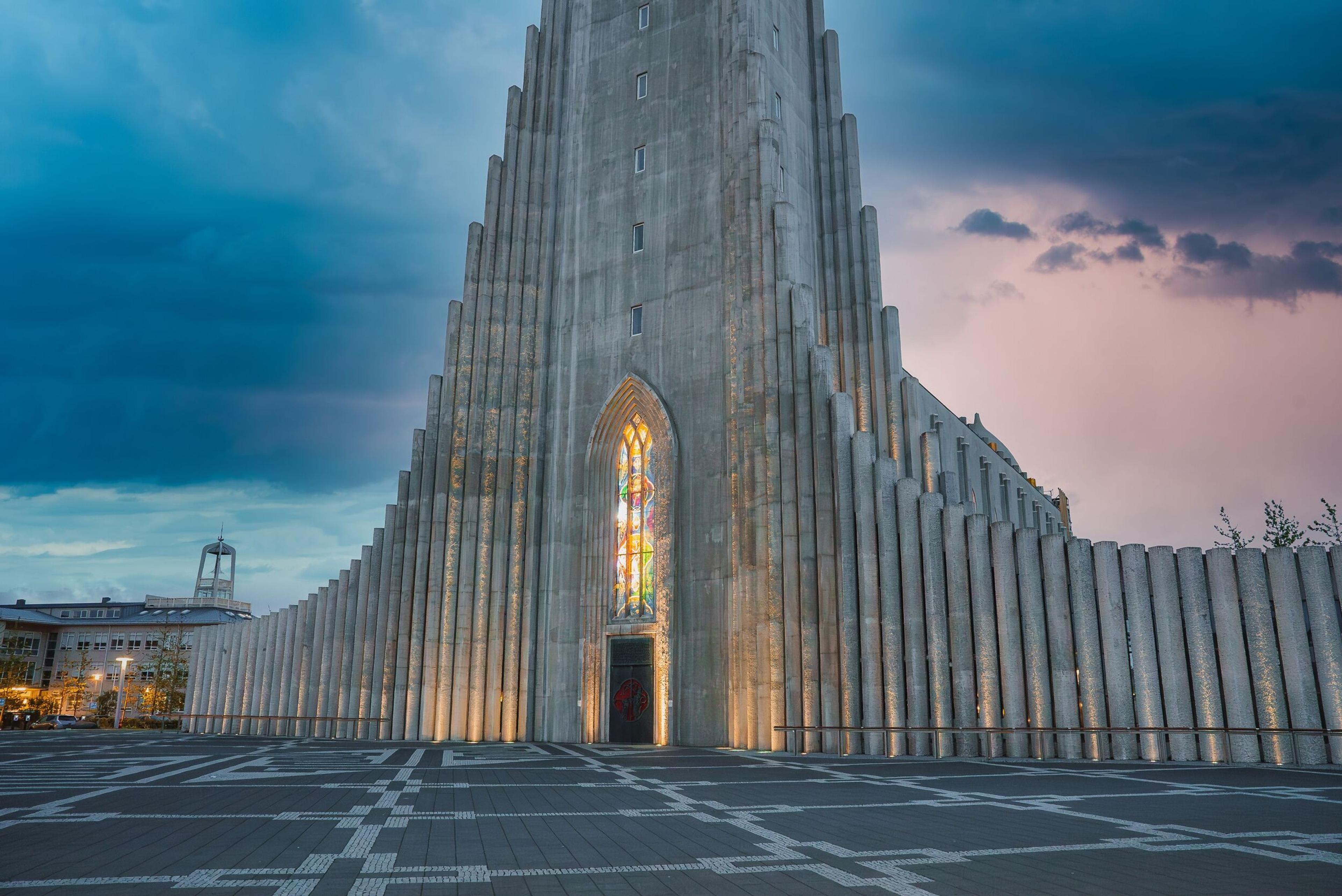 Hallgrímskirkja church, a tall concrete building with a fluted facade and colorful stained-glass window, illuminated at dusk.