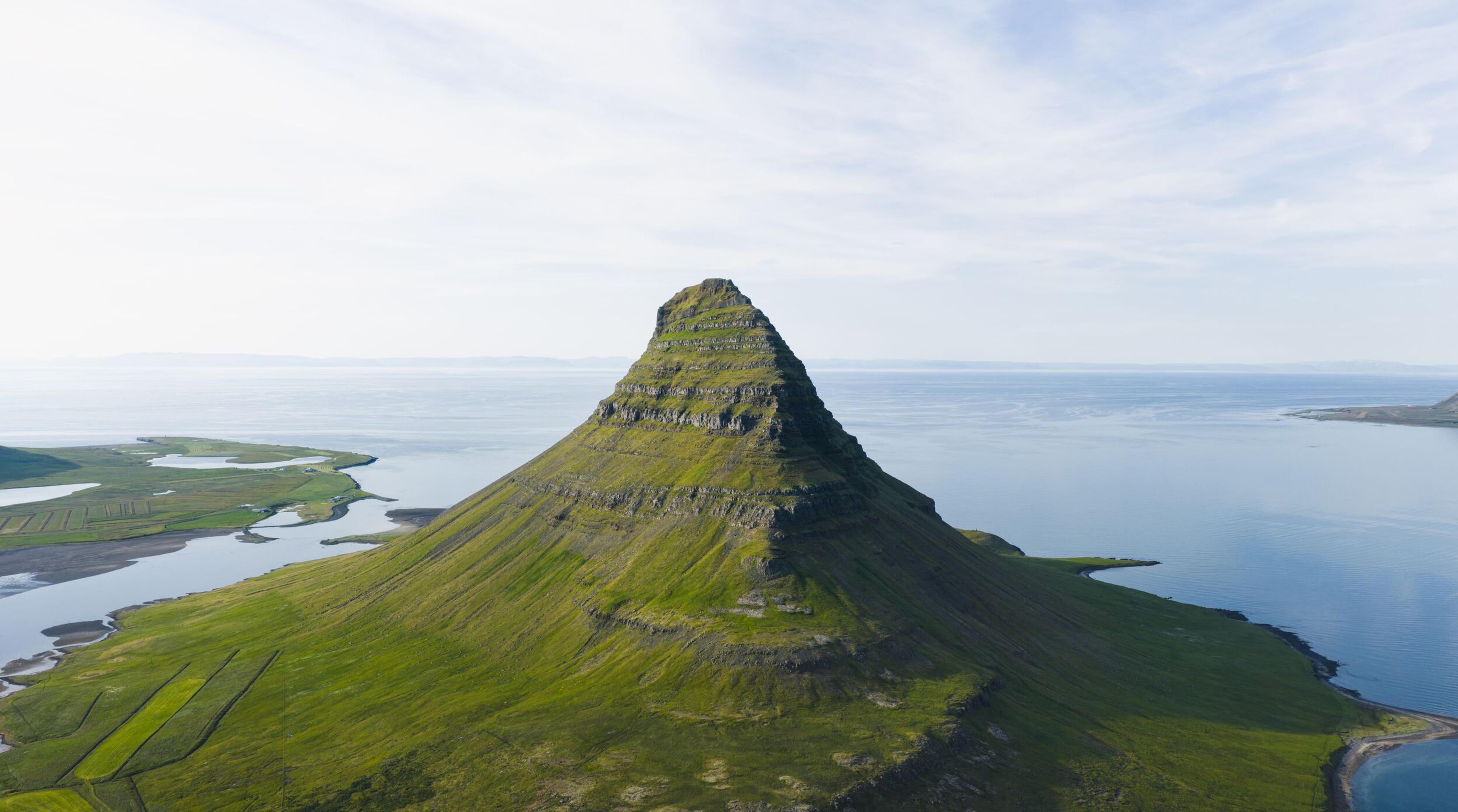 A green conical mountain (Kirkjufell) surrounded by water.