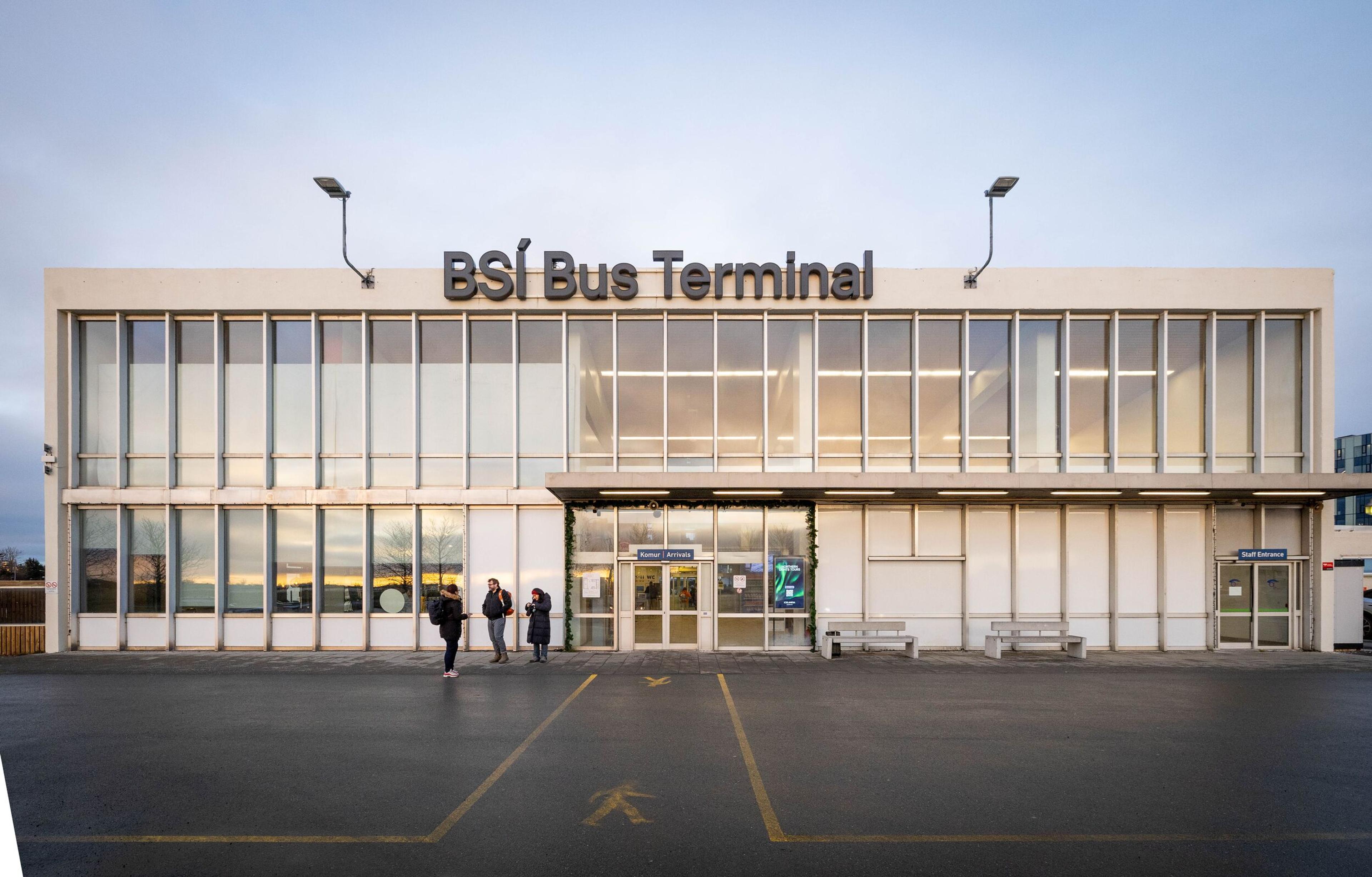 Exterior view of the BSÍ Bus Terminal, a modern two-story building with a glass facade, and a few people outside the entrance.