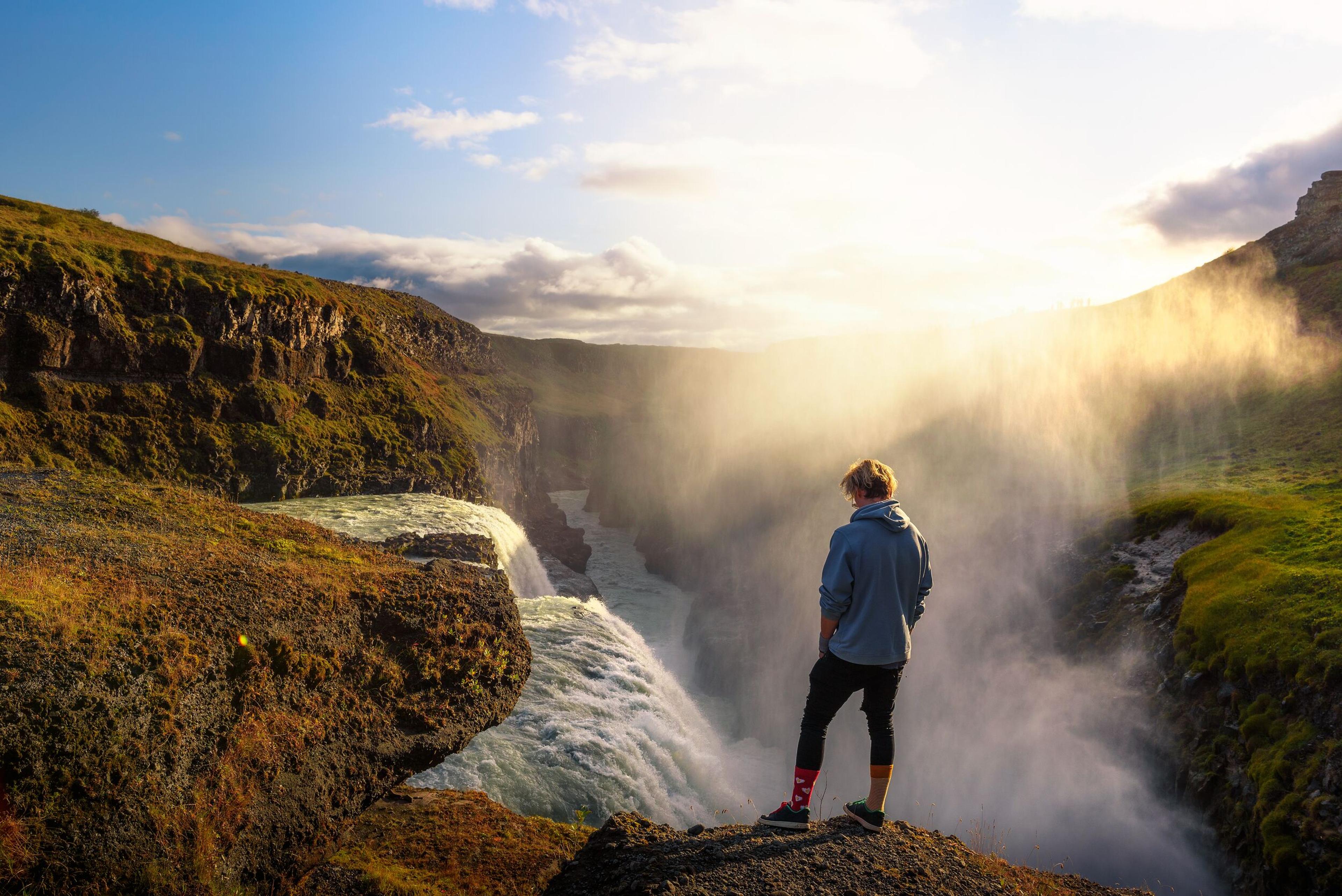 A person standing near the edge of Gullfoss waterfall in Iceland, enveloped in mist and bathed in golden sunlight.