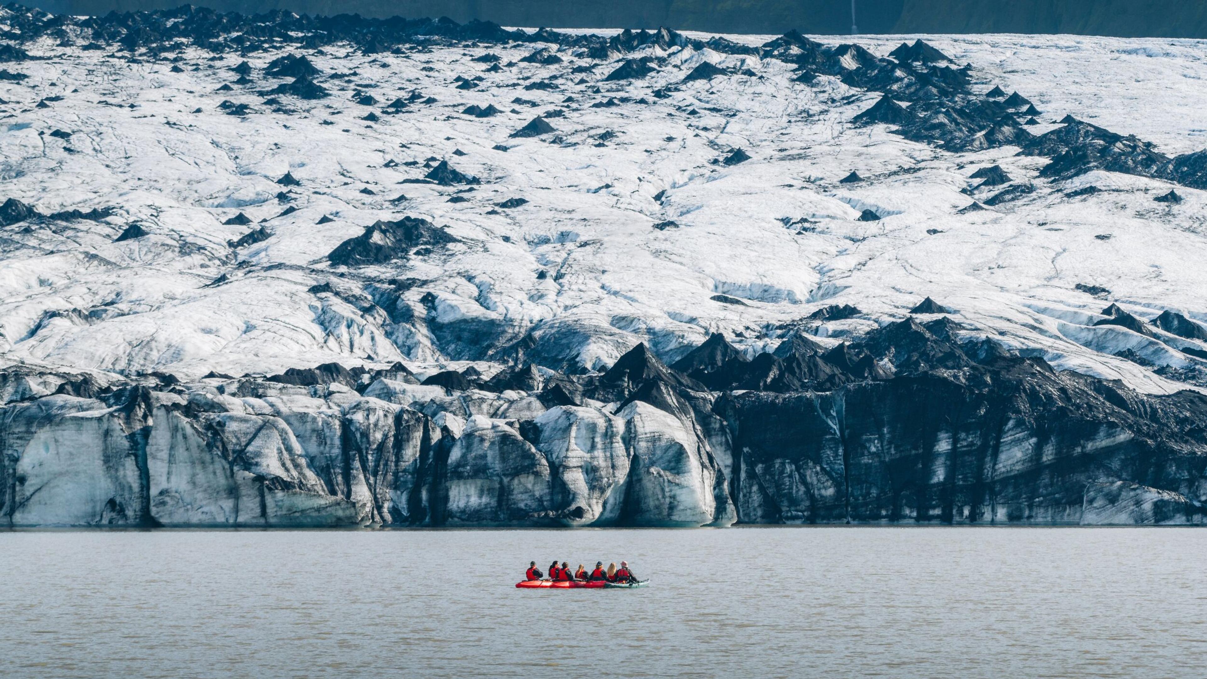 A red raft with people on a lake in front of a large glacier.