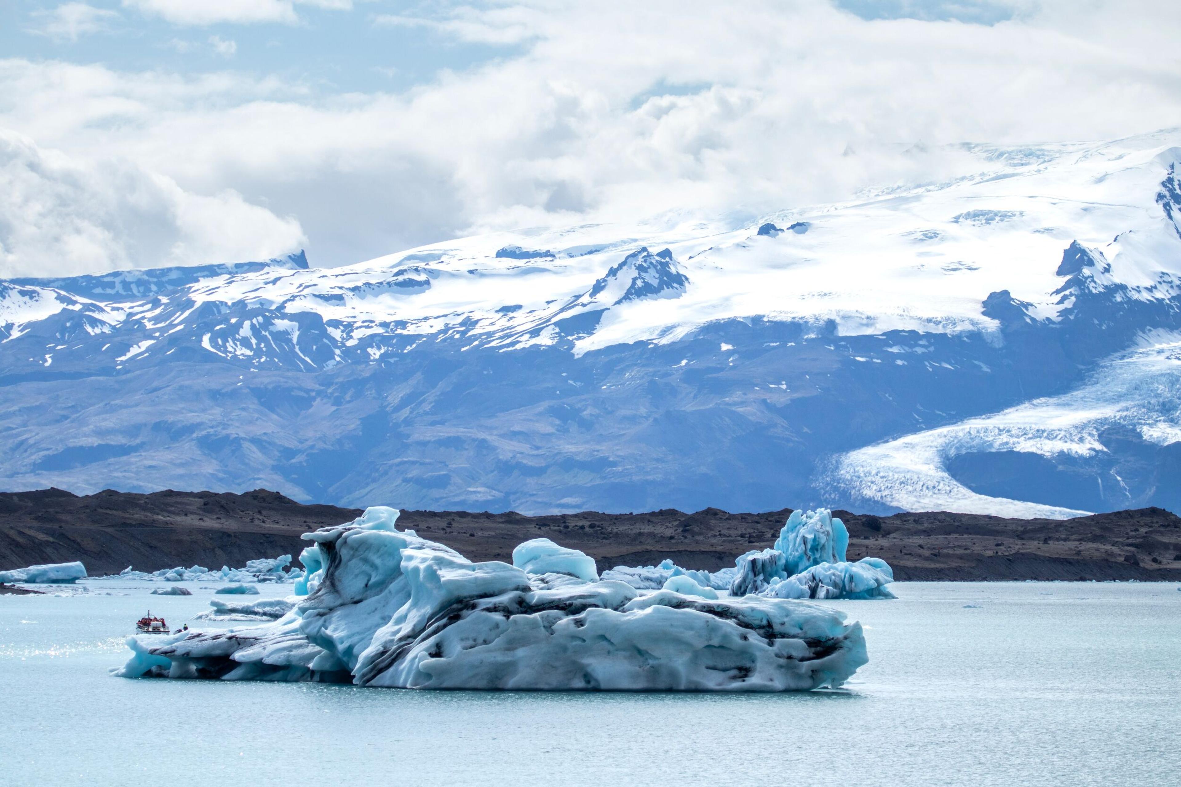 Blue and white icebergs in a glacial lake with snow-capped mountains and glaciers in the background.