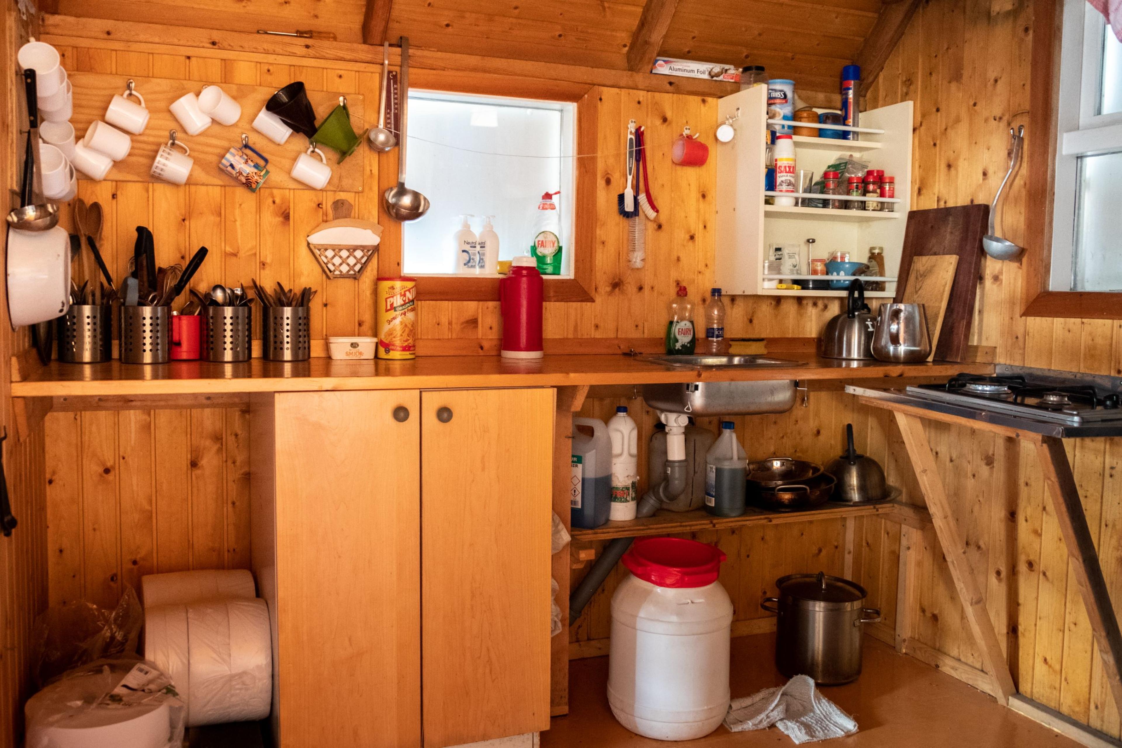 Interior of a wooden hut showcasing a compact kitchen area, complete with utensils and assorted items.