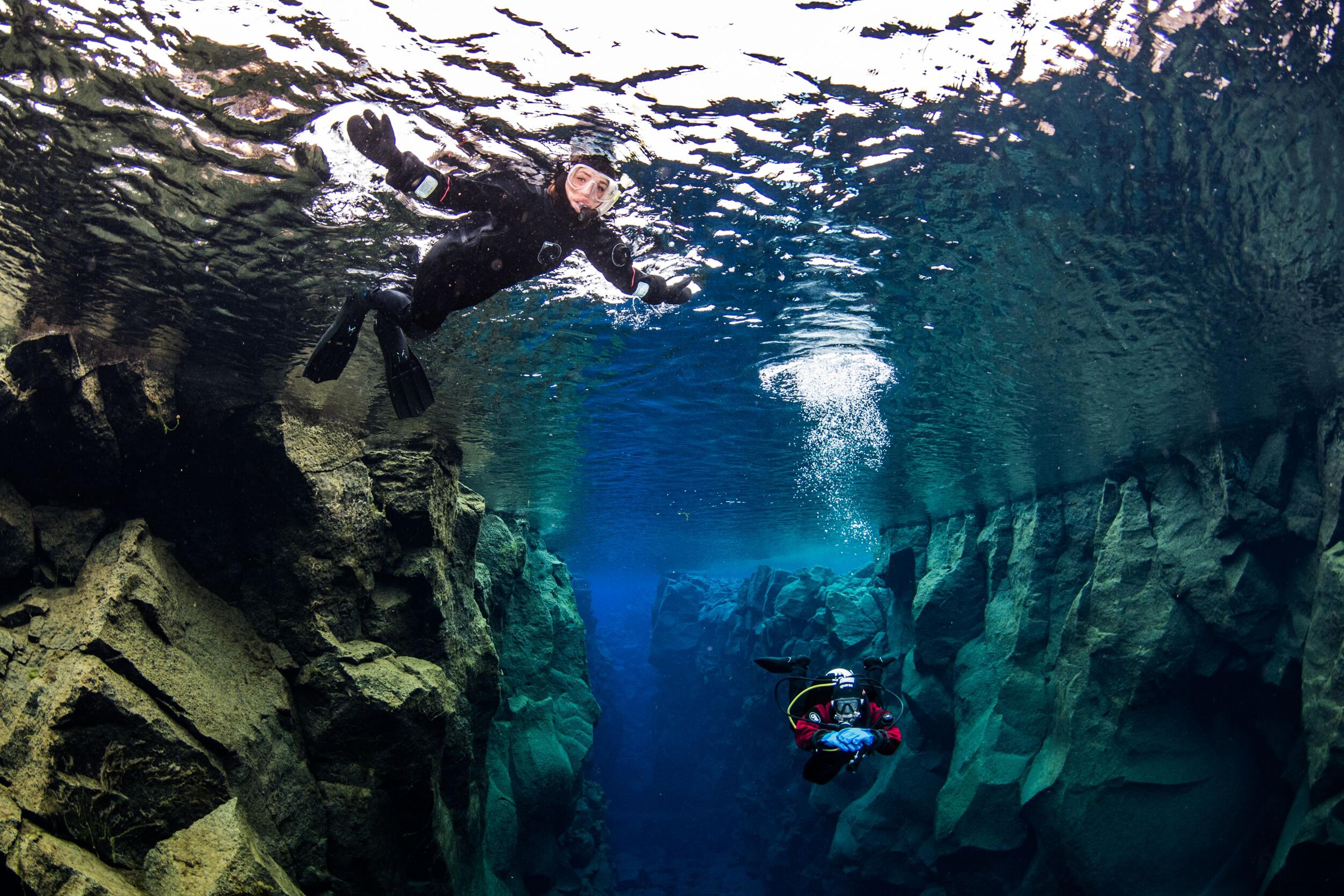 Two divers exploring the crystal-clear waters and underwater rock formations at Silfra in Thingvellir National Park.