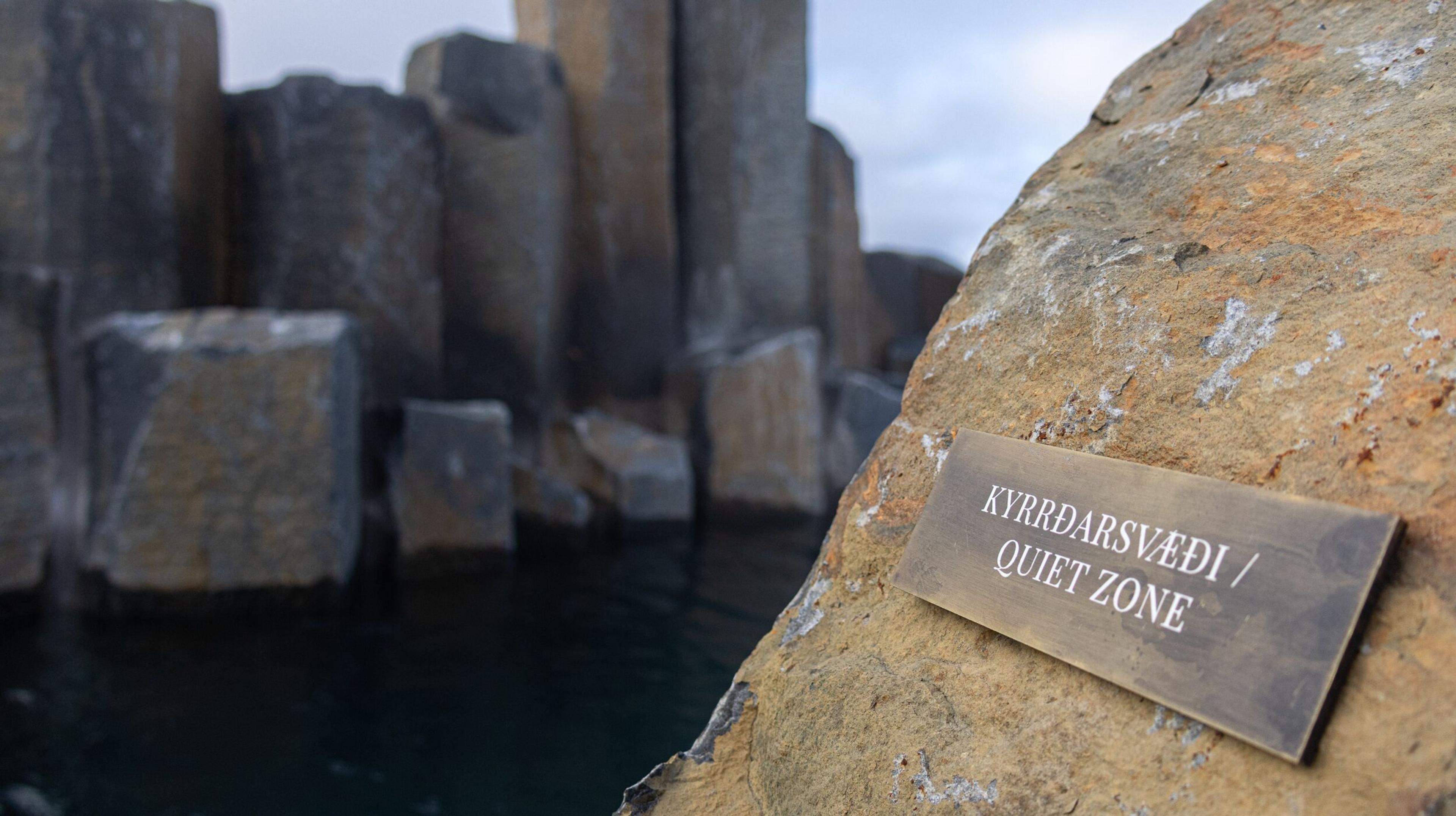 A "QUIET ZONE" sign on a rock, with blurred basalt columns rising from dark water in the background.