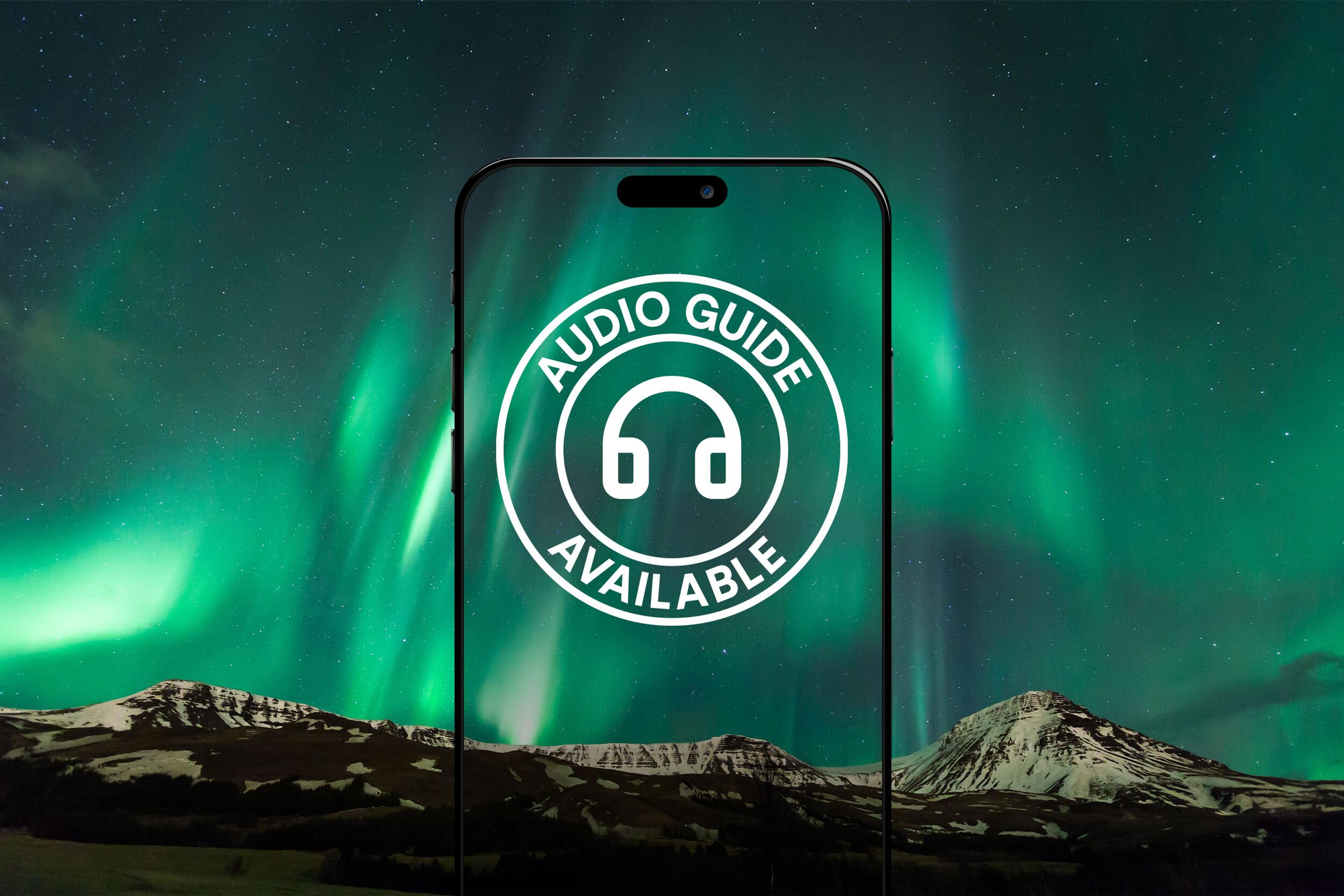 A smartphone displaying an "AUDIO GUIDE AVAILABLE" icon against a backdrop of the Northern Lights over snowy mountains.