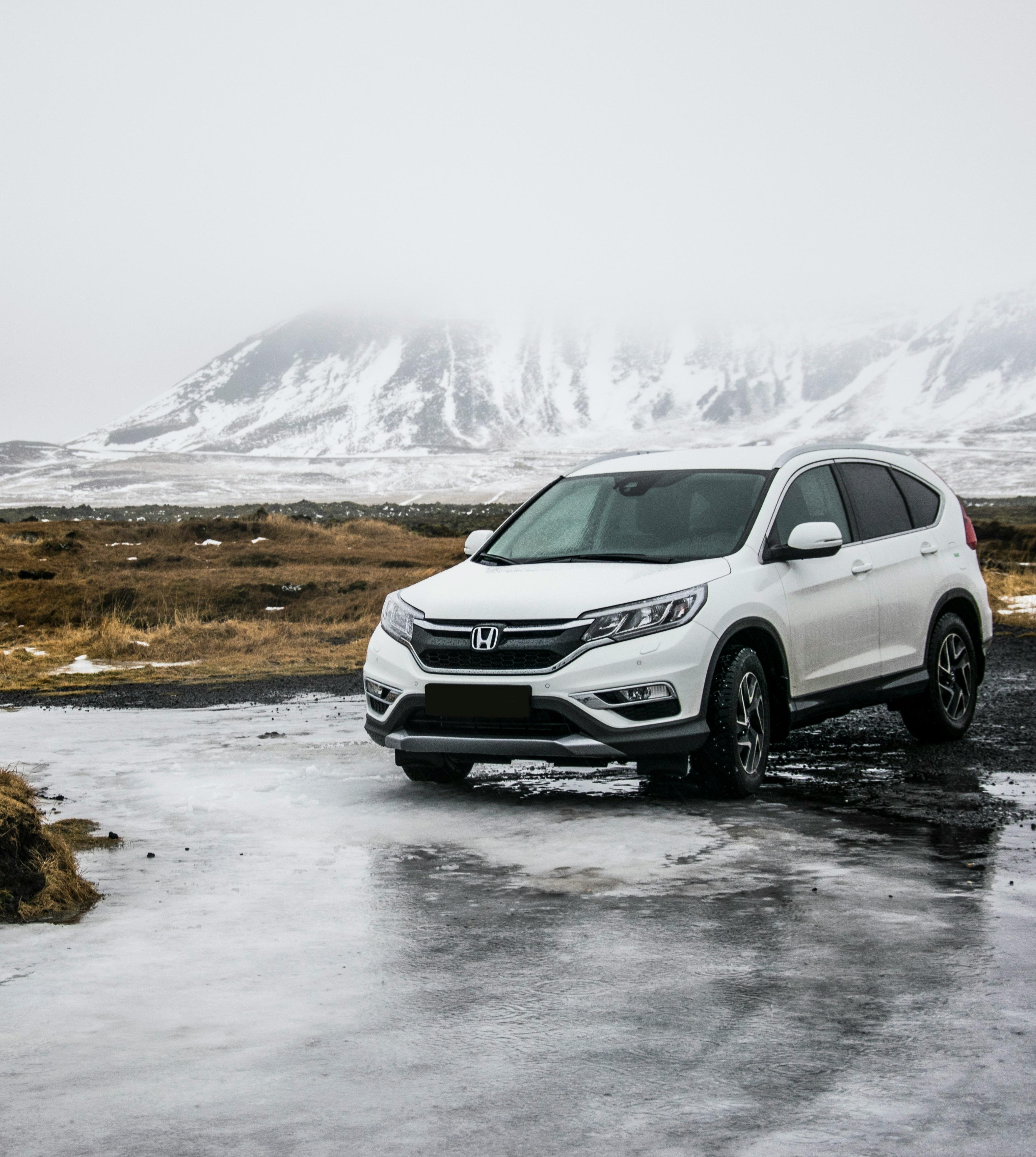 A white SUV parked on an icy road with snow-covered mountains in the background.