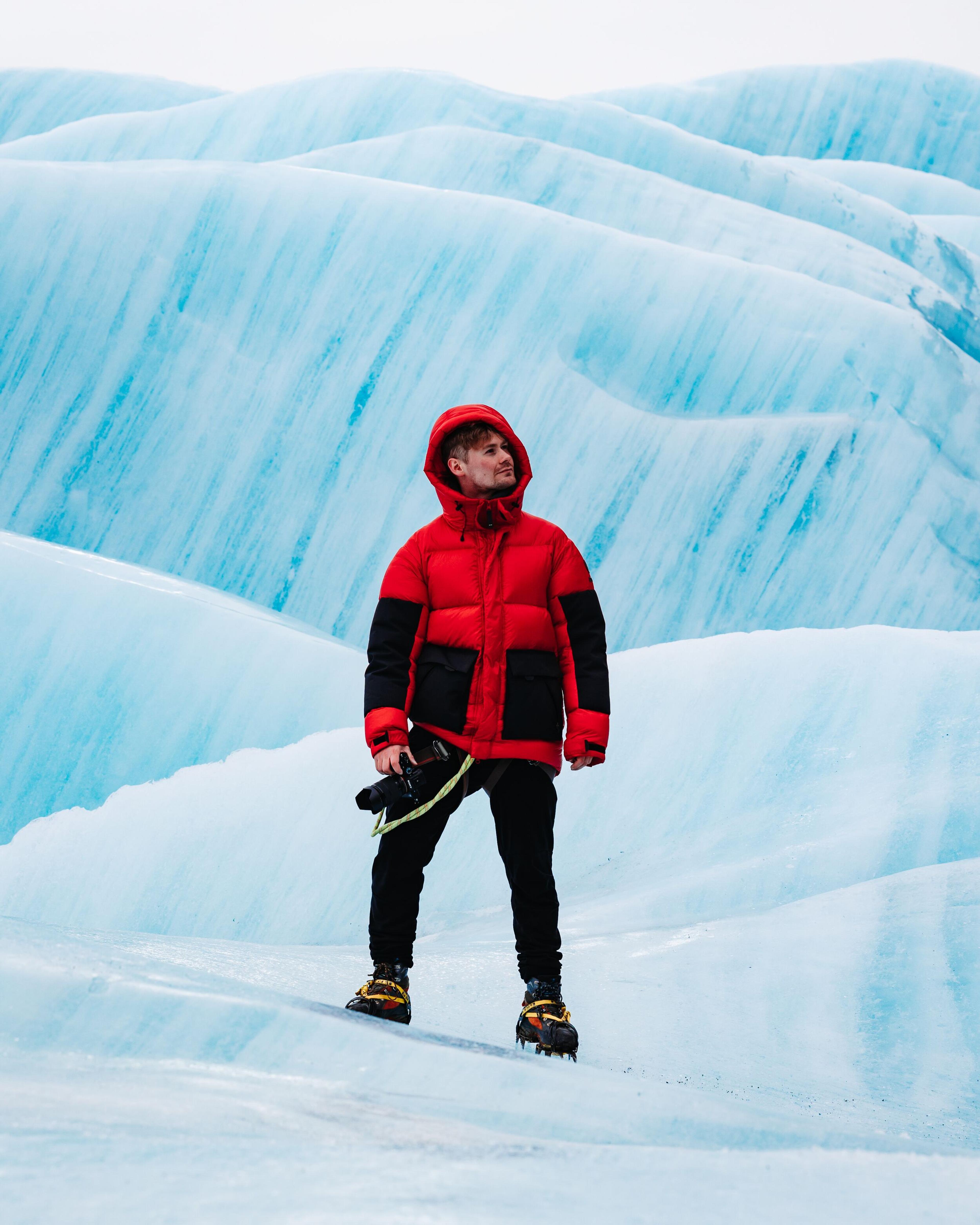 A person in a thick parka standing atop a vast blue glacier.