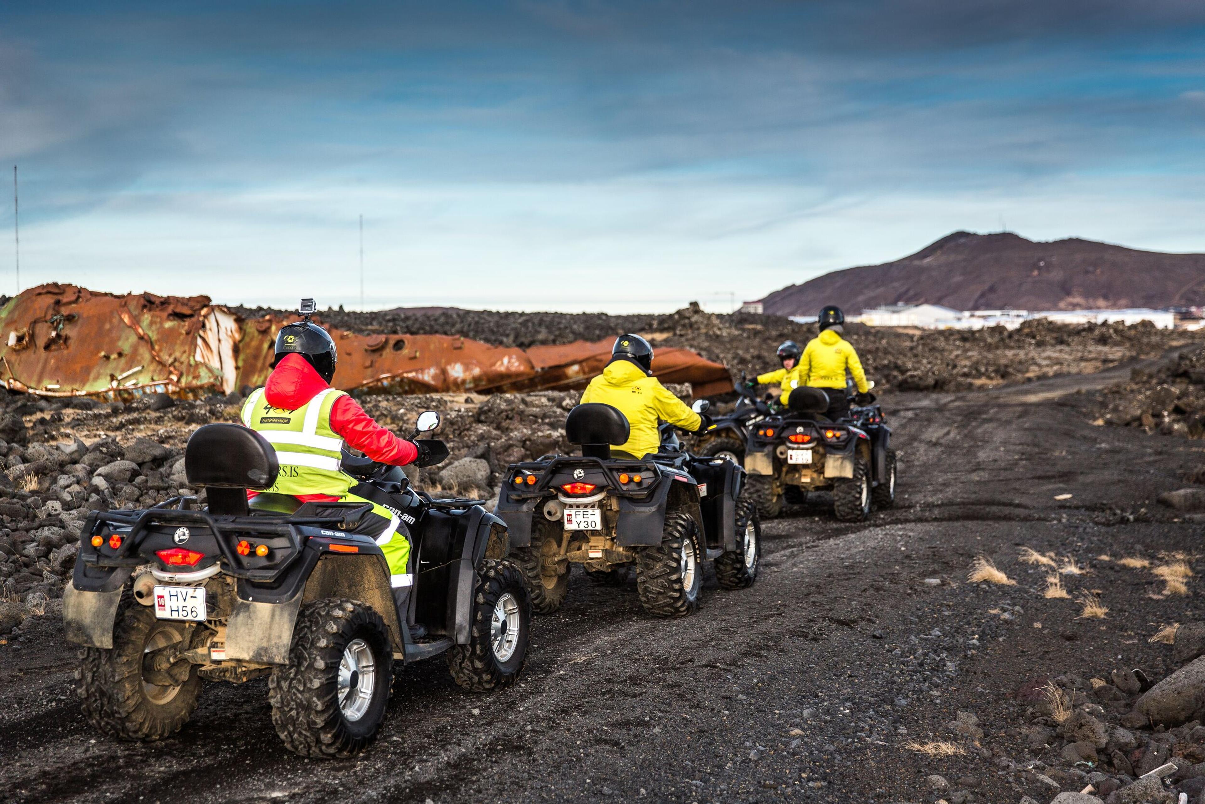three people riding ATVs on a gravel road in Iceland.