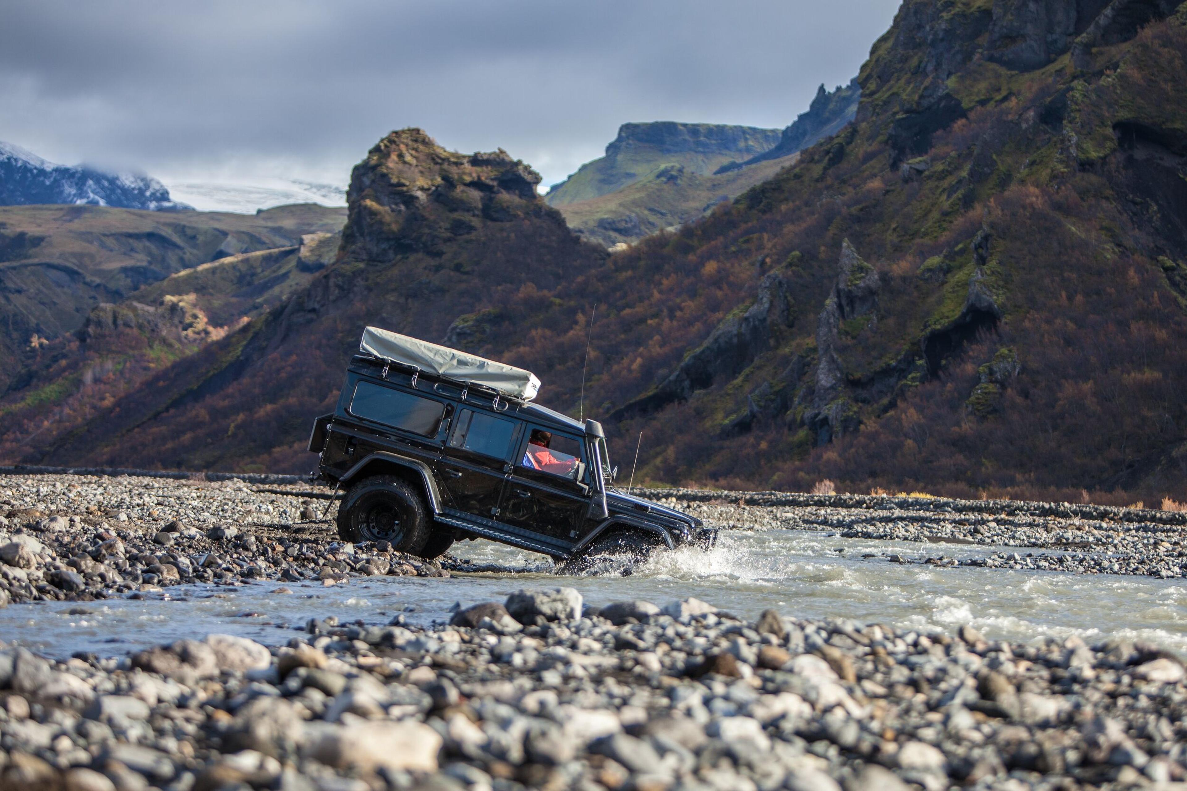 Large jeep navigating a river amidst untamed wilderness.