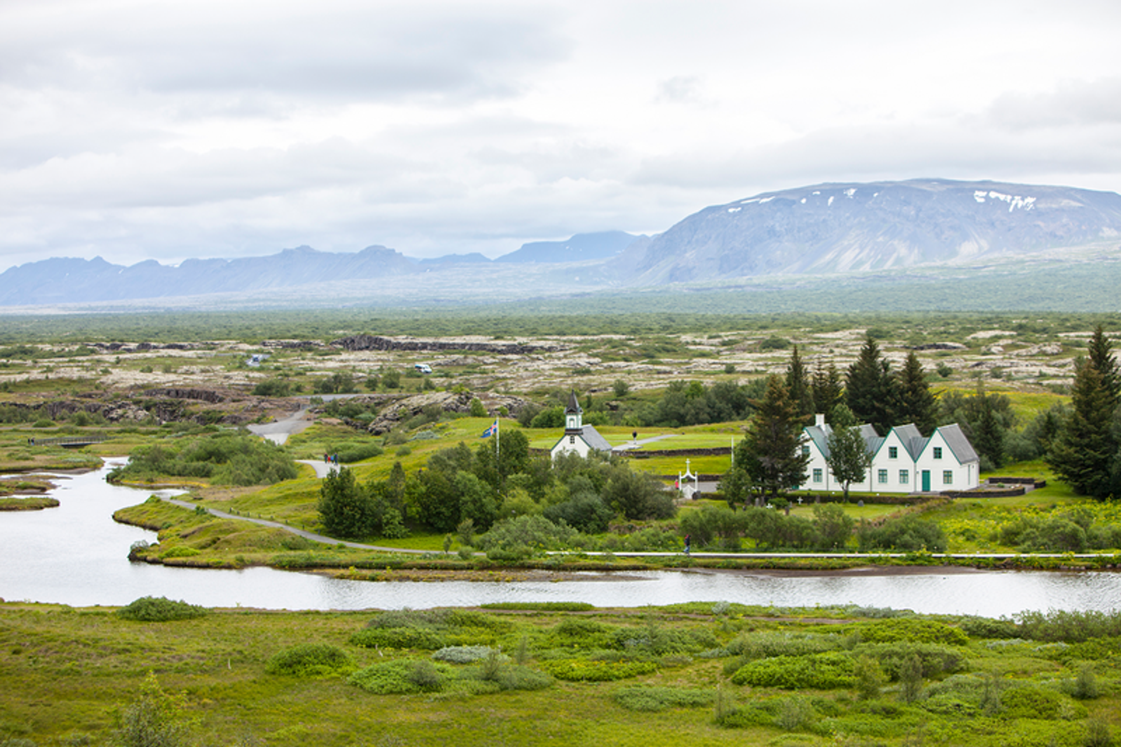 a white house sits in the middle of a lush green field with mountains in the background