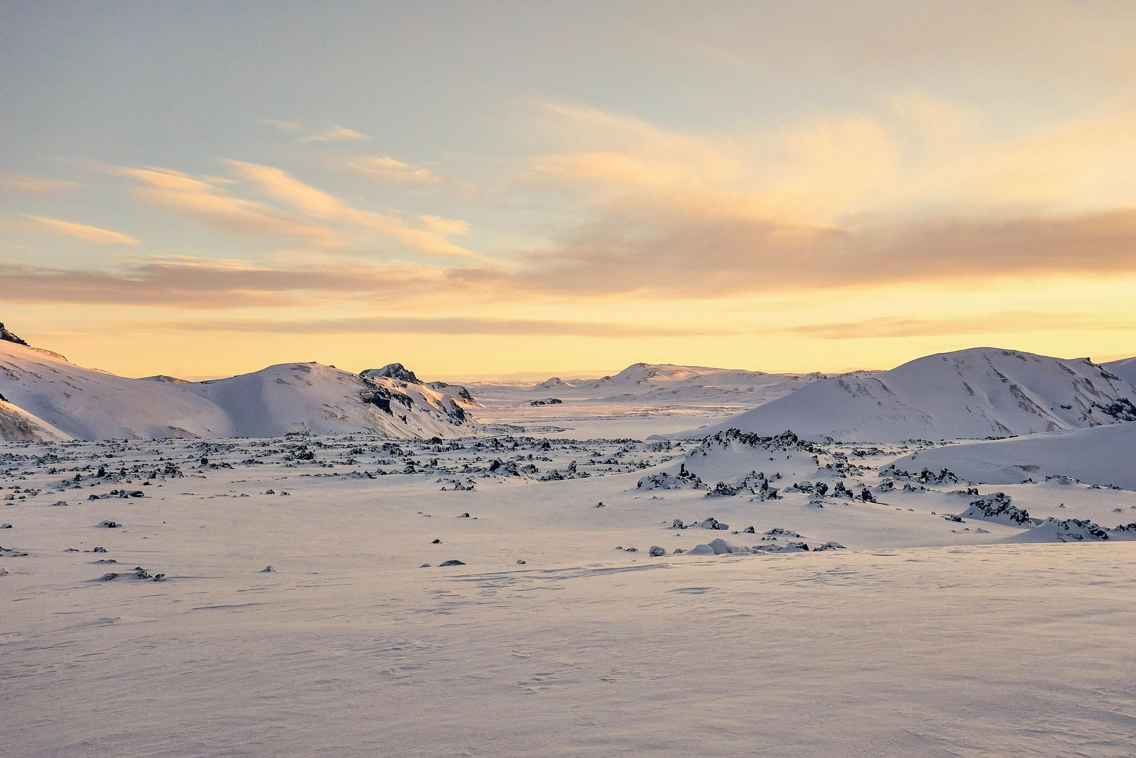 A breathtaking winter scene in Landmannalaugar with a golden sunset illuminating snow-covered mountains and rugged volcanic terrain.