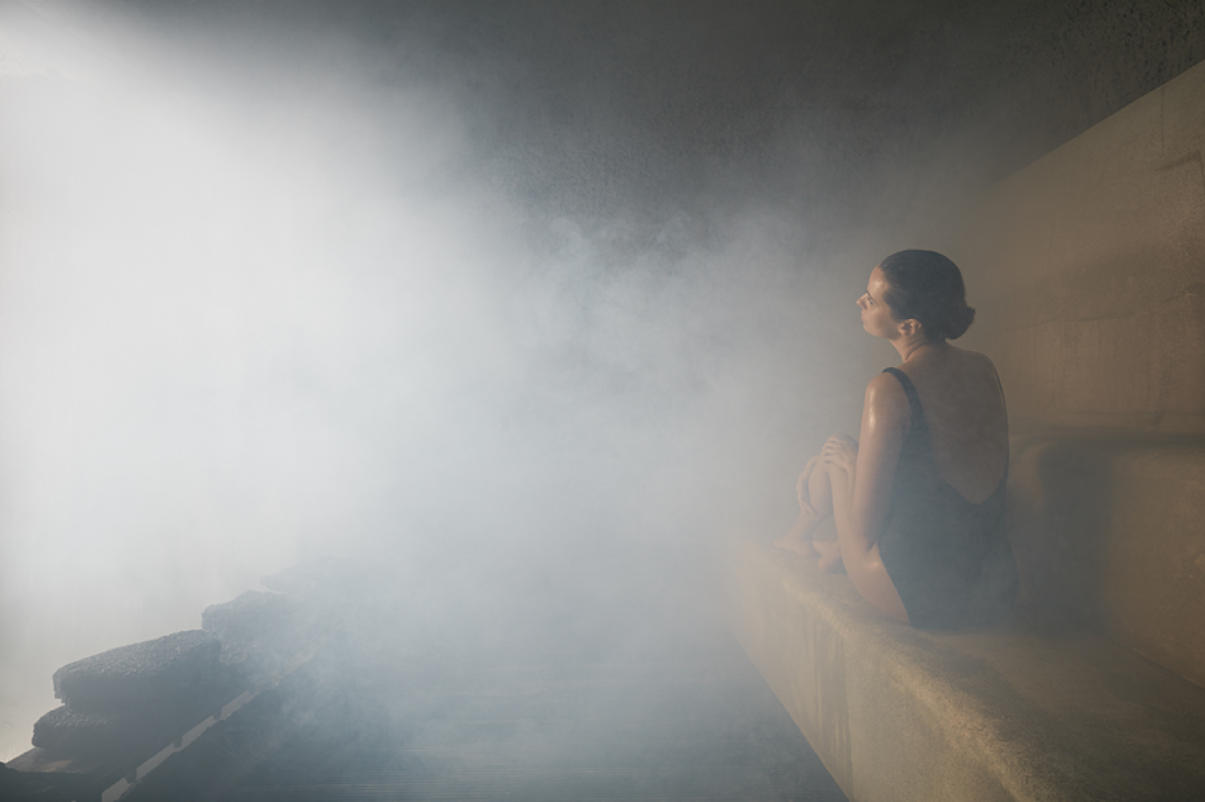 Woman relaxing in a steam room, enveloped in warm mist.
