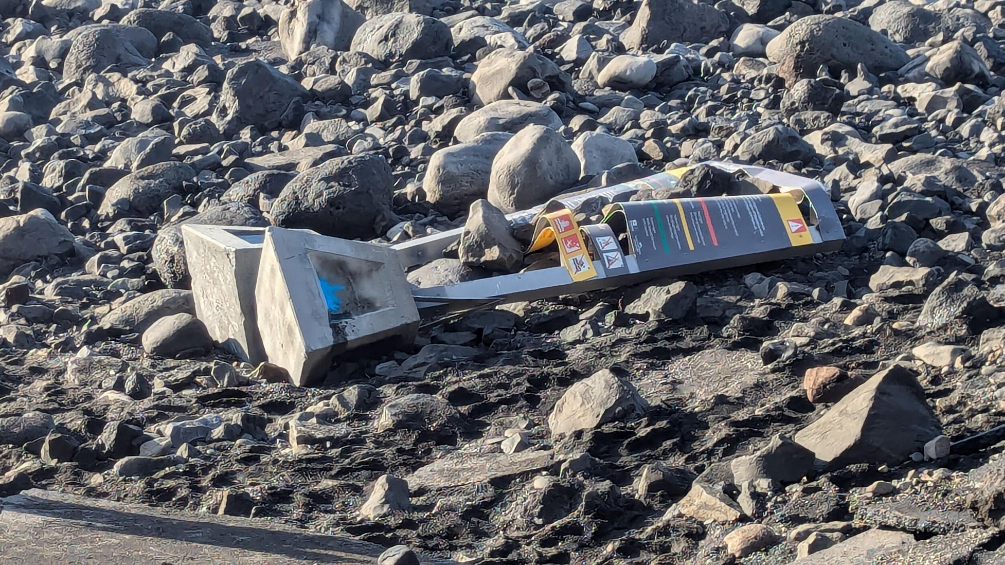 A broken sign with a concrete base and black panel lies on dark, rocky ground.