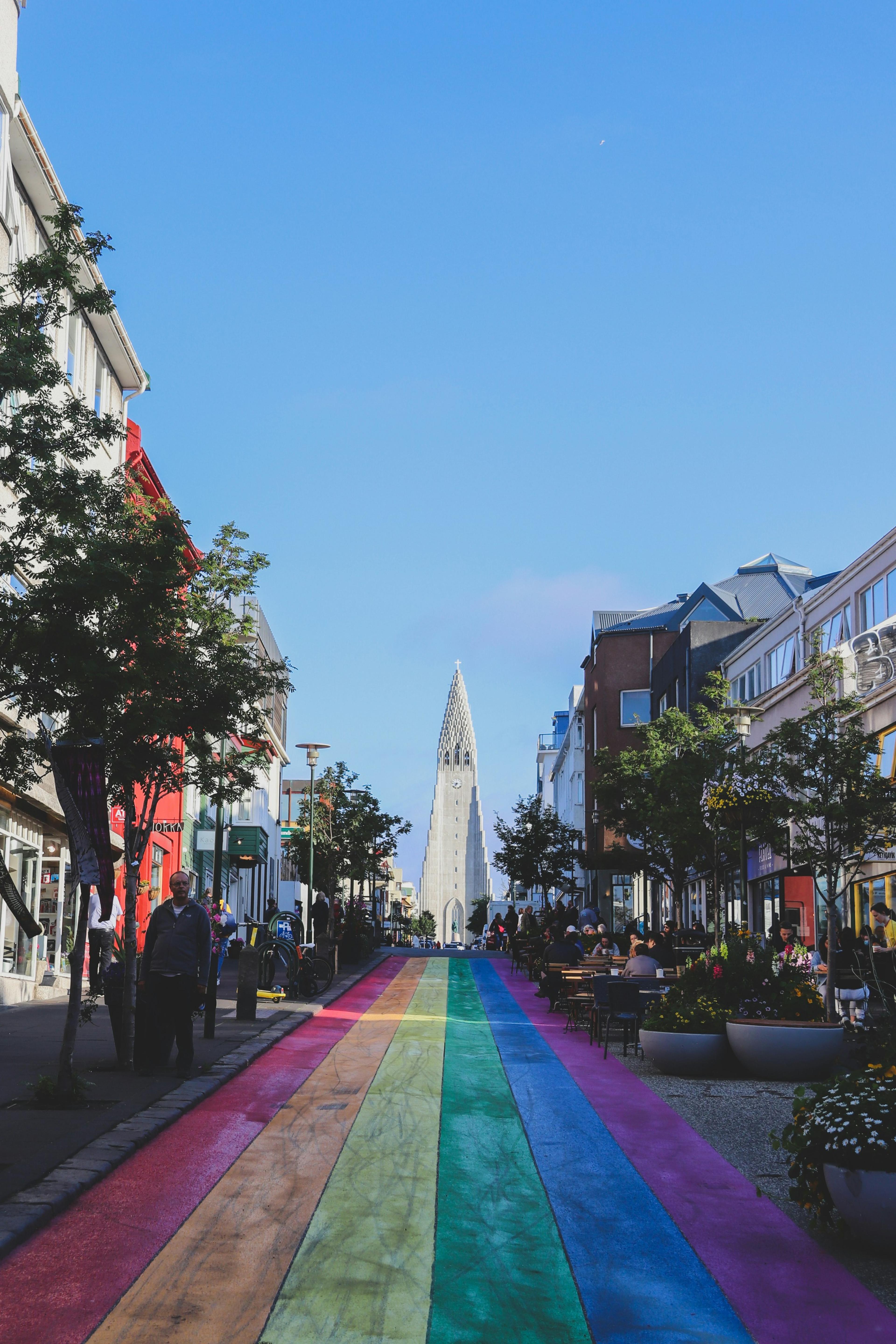 Hallgrímskirkja Church in Reykjavík, viewed from a colorful rainbow street filled with people.