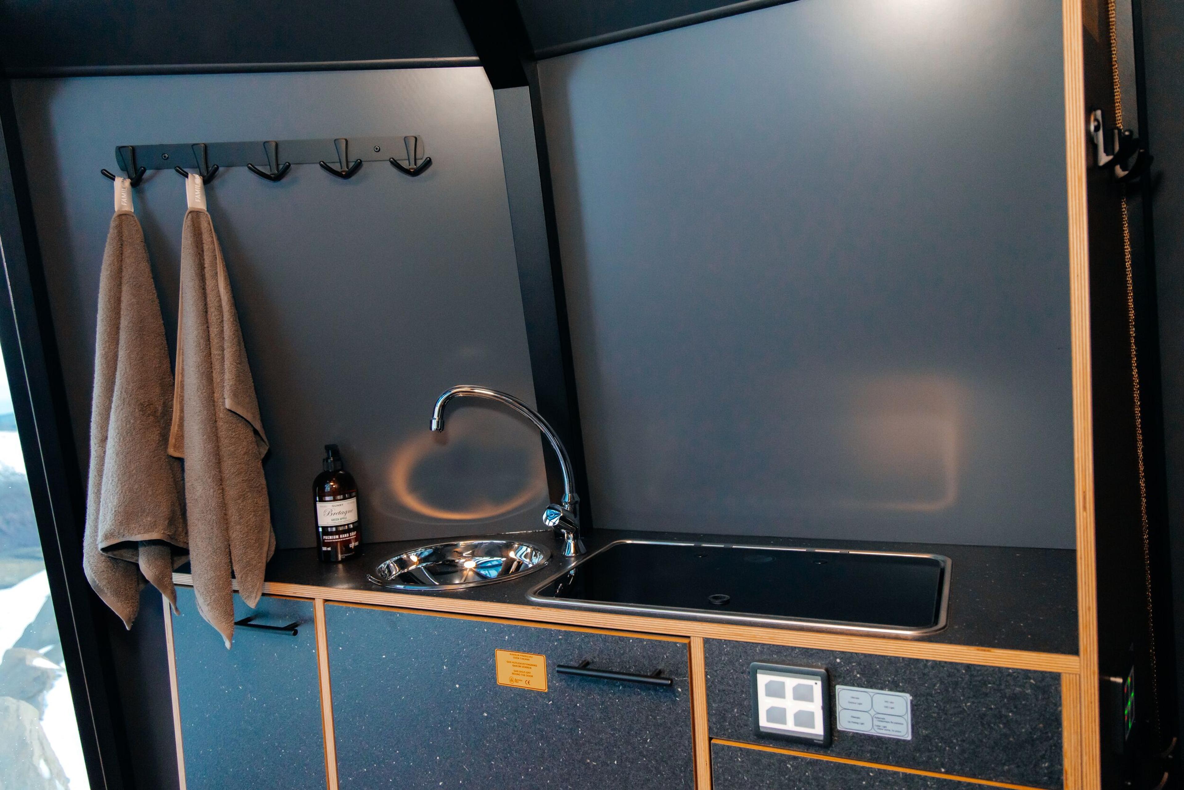 A modern, compact kitchen with a sink, induction cooktop, dark cabinetry, and two towels on hooks.
