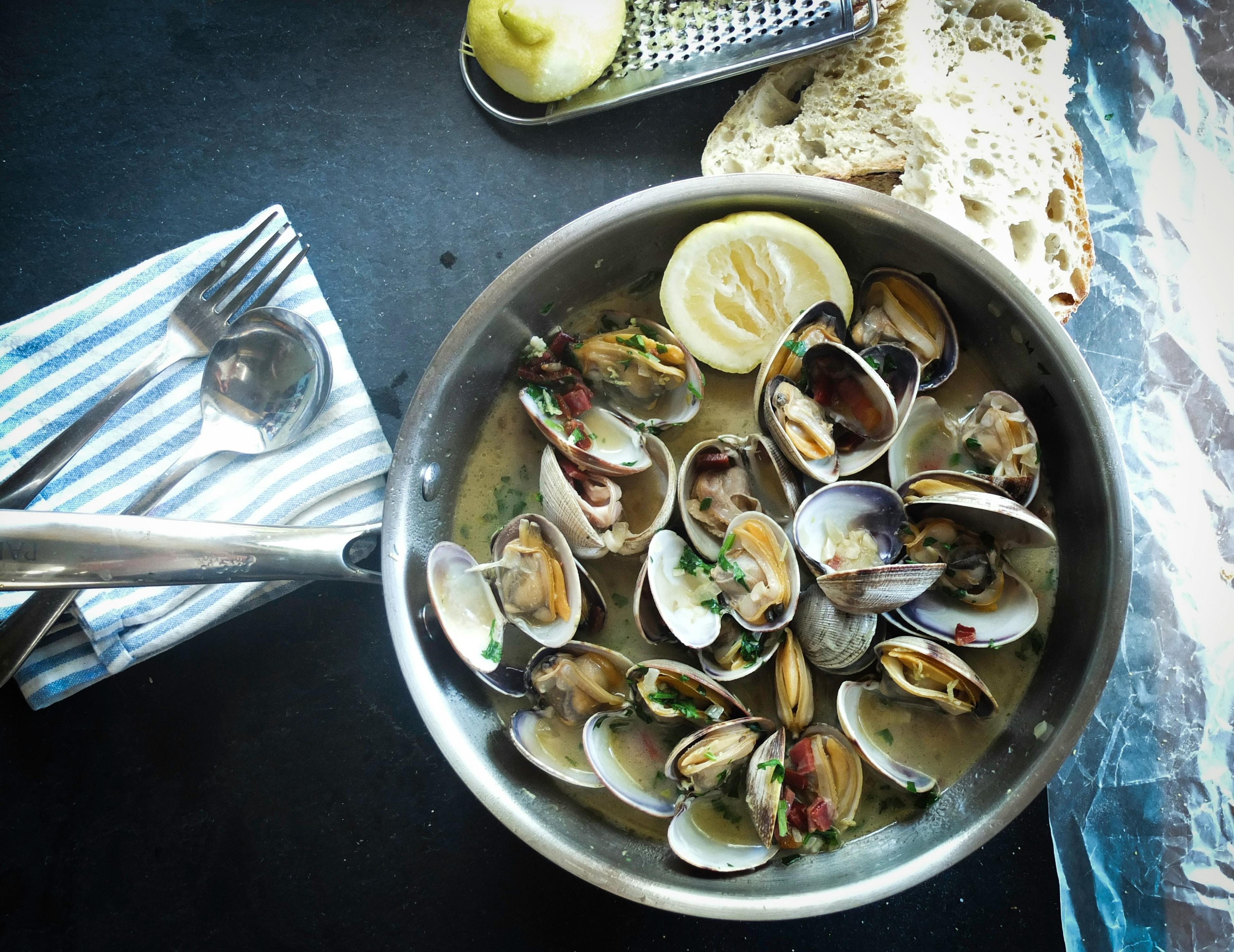 A skillet filled with steamed clams, garnished with herbs and lemon slices, accompanied by bread, featured in an Iceland food walk.