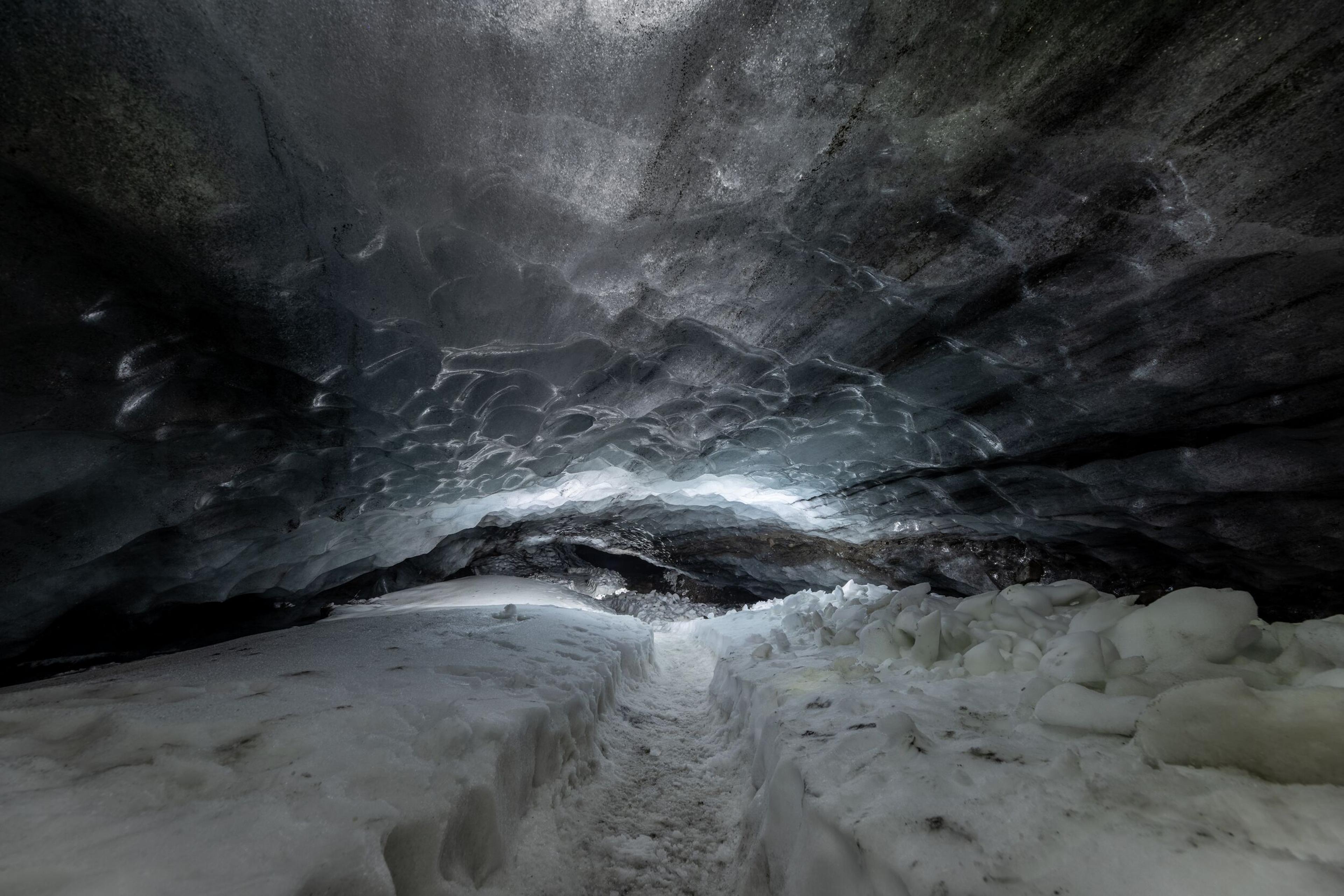 Empty pathway inside Askur ice cave, with textured ice ceiling and snow-covered ground.