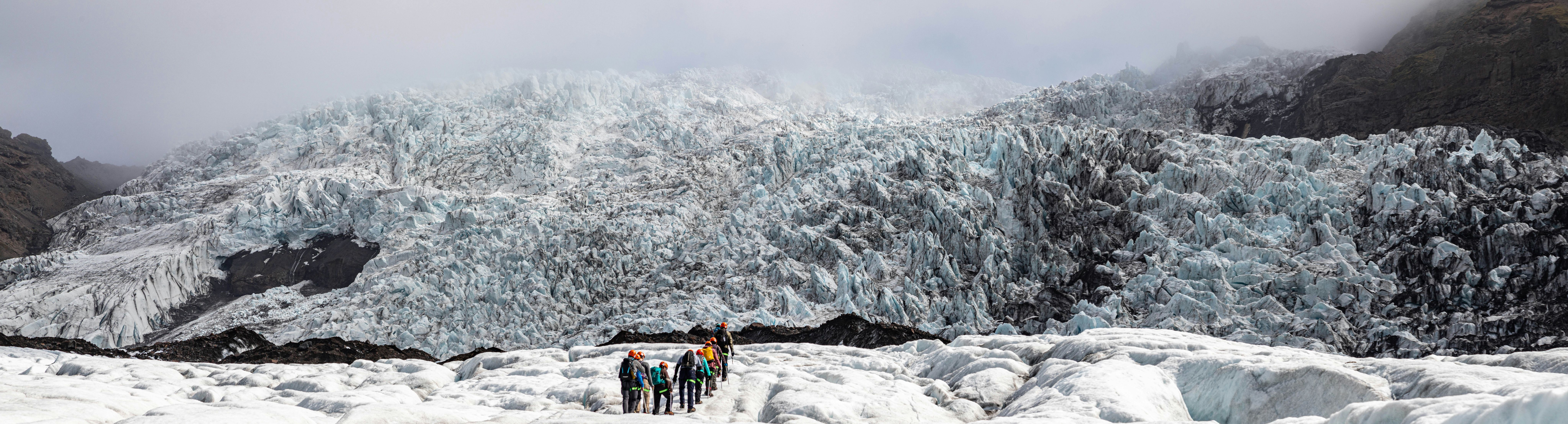 Group of climbers ascending an icy slope toward a massive, jagged glacier in the Icelandic Highlands.