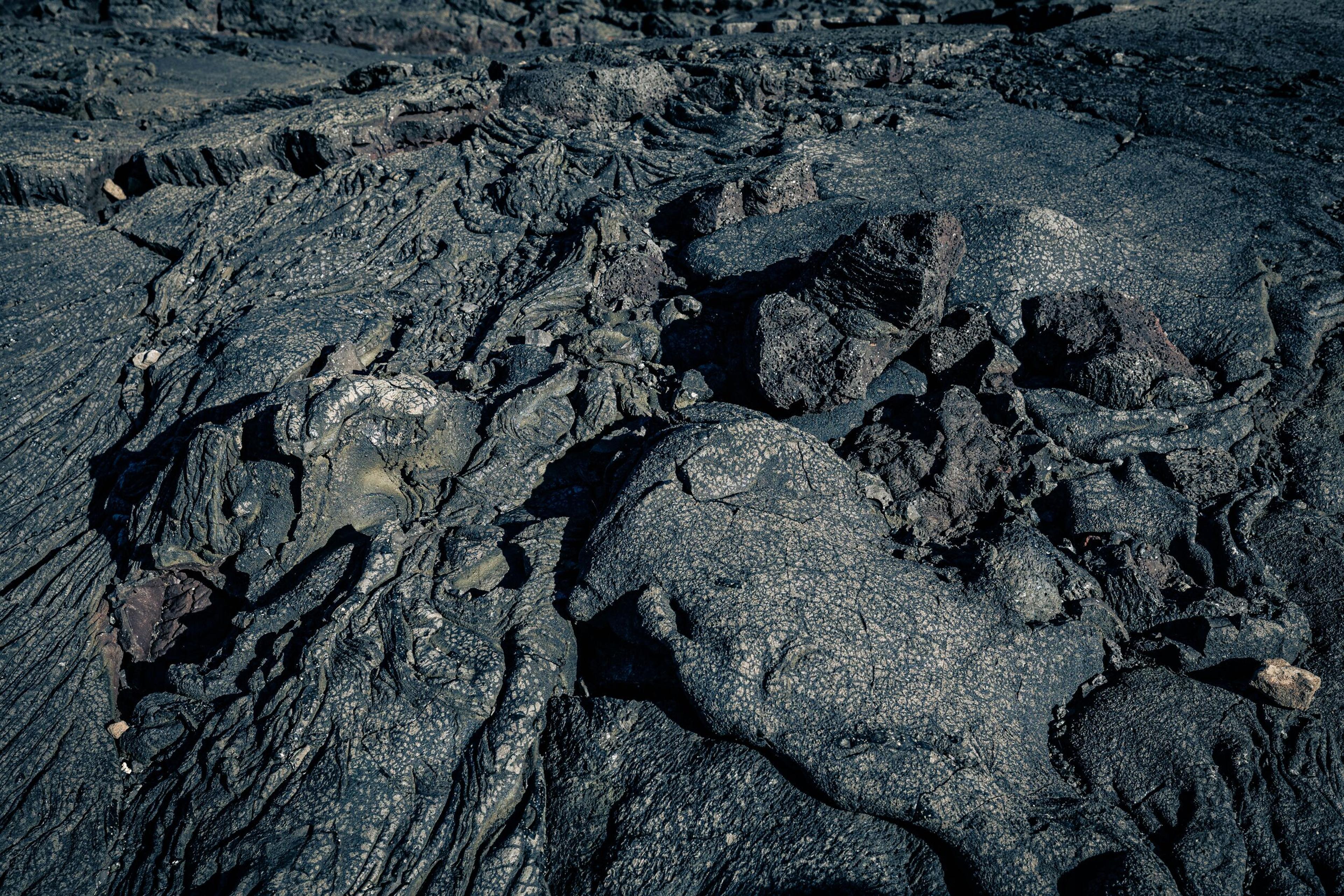 Close-up of solidified lava rocks with rugged textures and dark, uneven surfaces, highlighting volcanic geological formations.