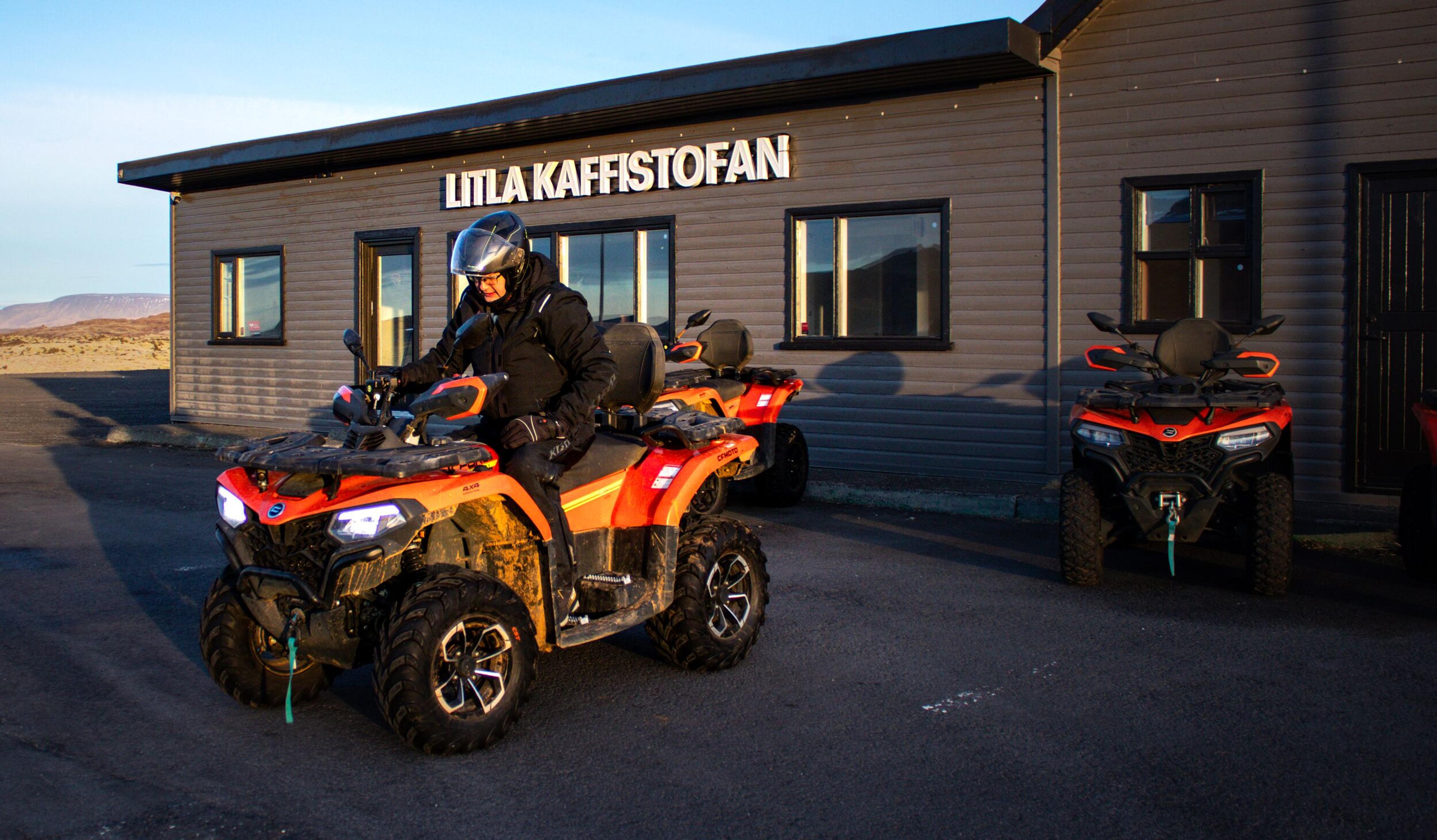 A person on an orange ATV in front of a building named "LITLA KAFFISTOFAN" with other ATVs parked.