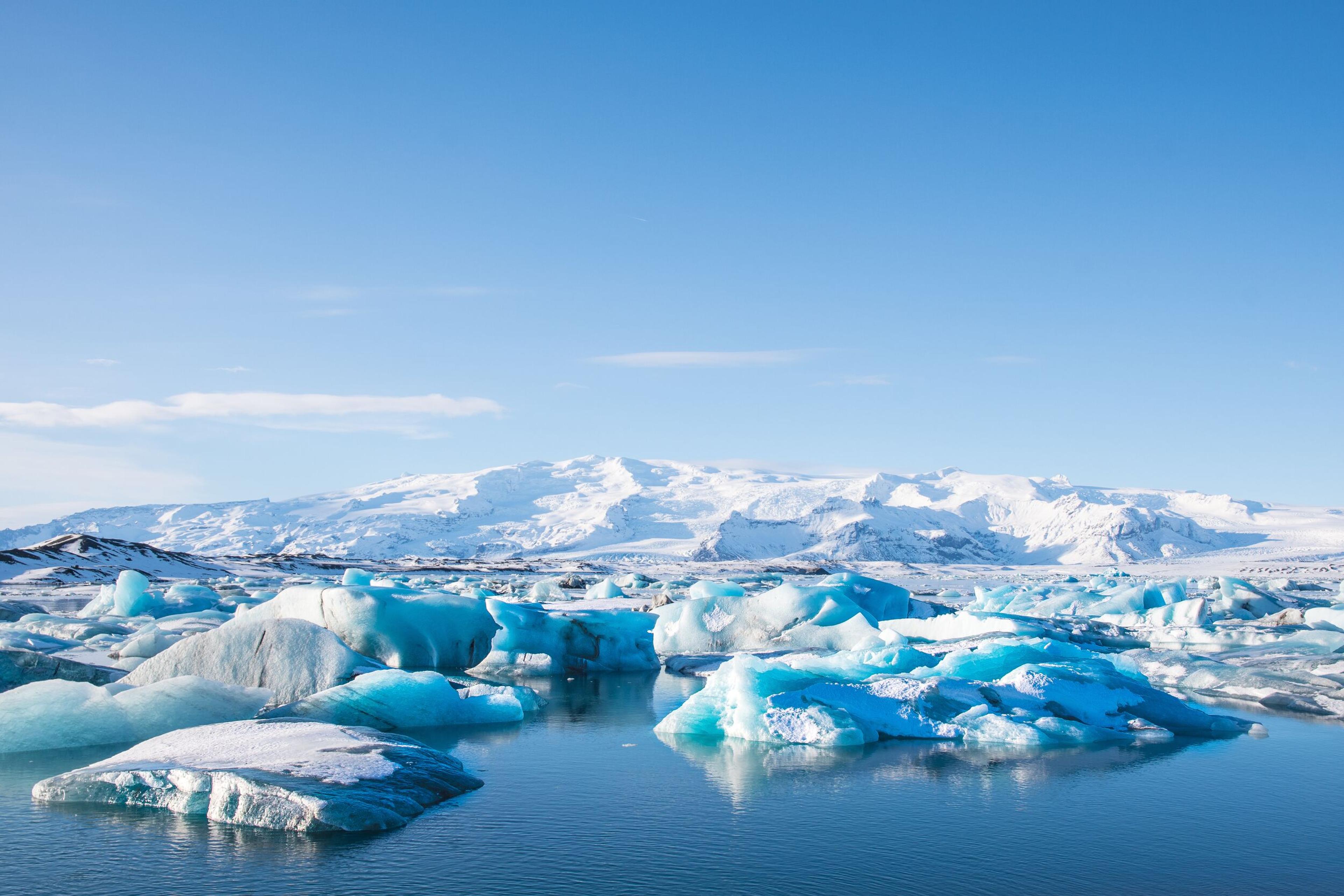 Blue icebergs floating in a glacial lagoon with snow-covered mountains in the background.
