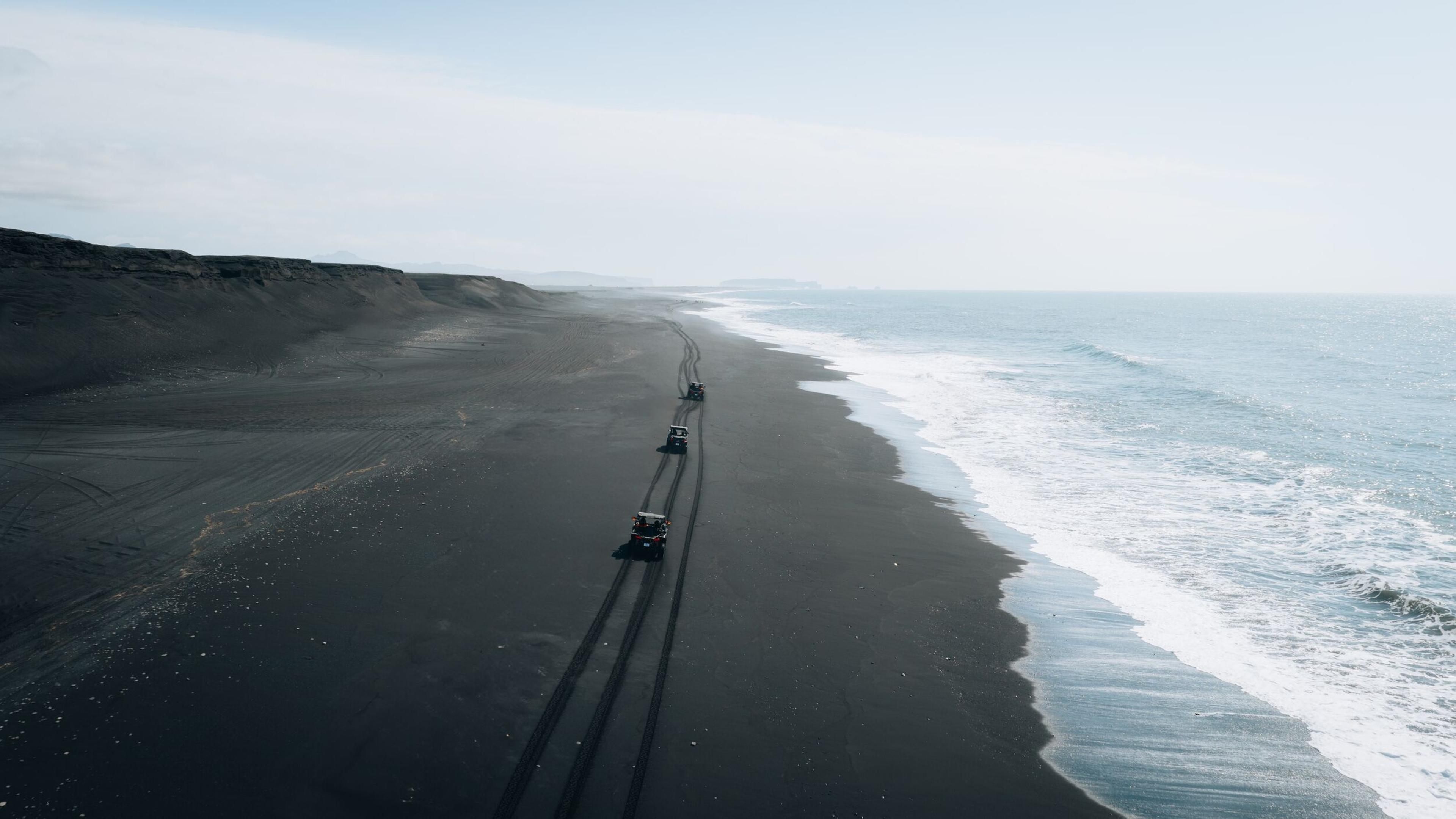 a group of people are riding atvs on a black sandy beach near the ocean .
