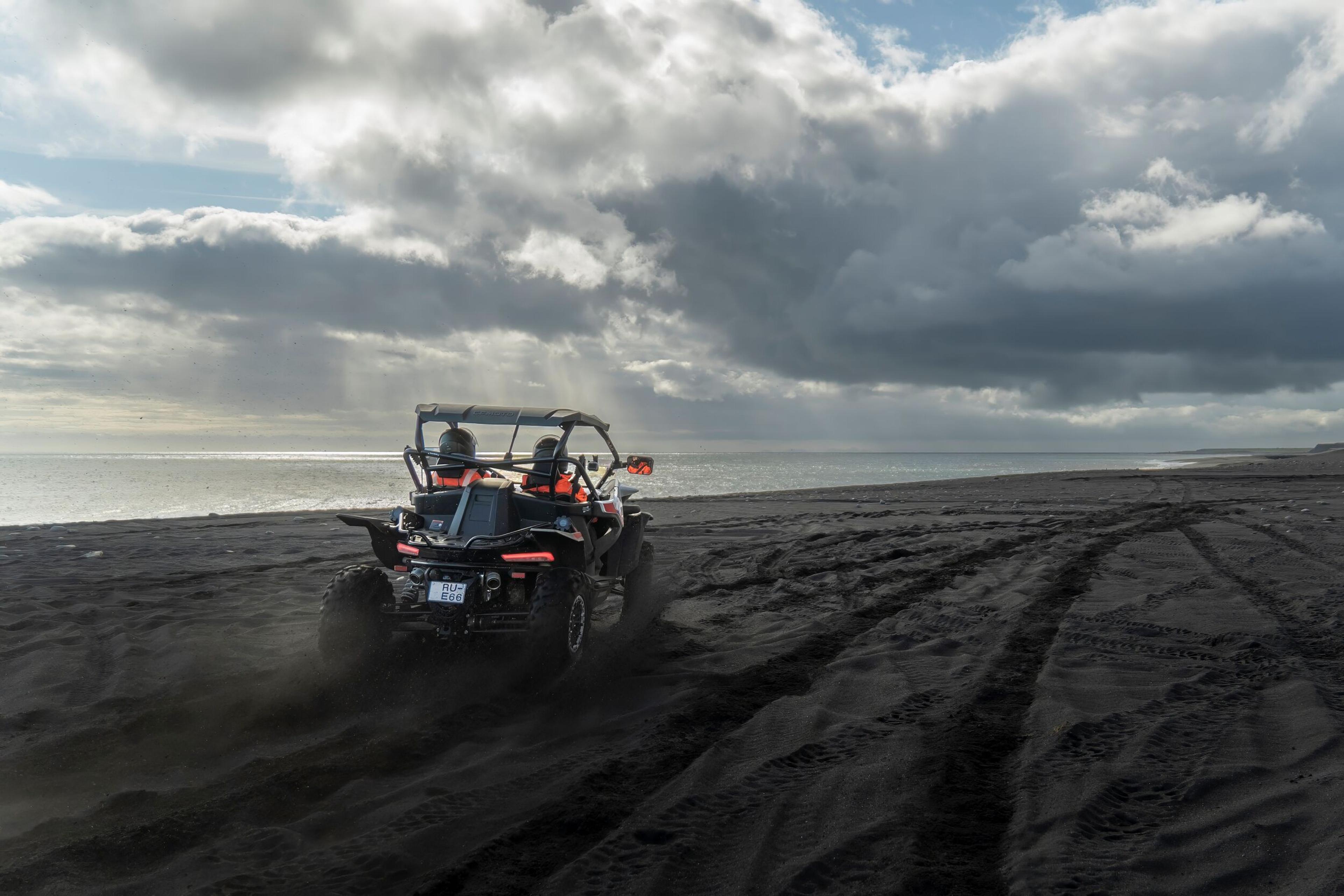 An ATV racing along a black sand beach under a dramatic sky in South Iceland, highlighting exciting outdoor activities in the area.