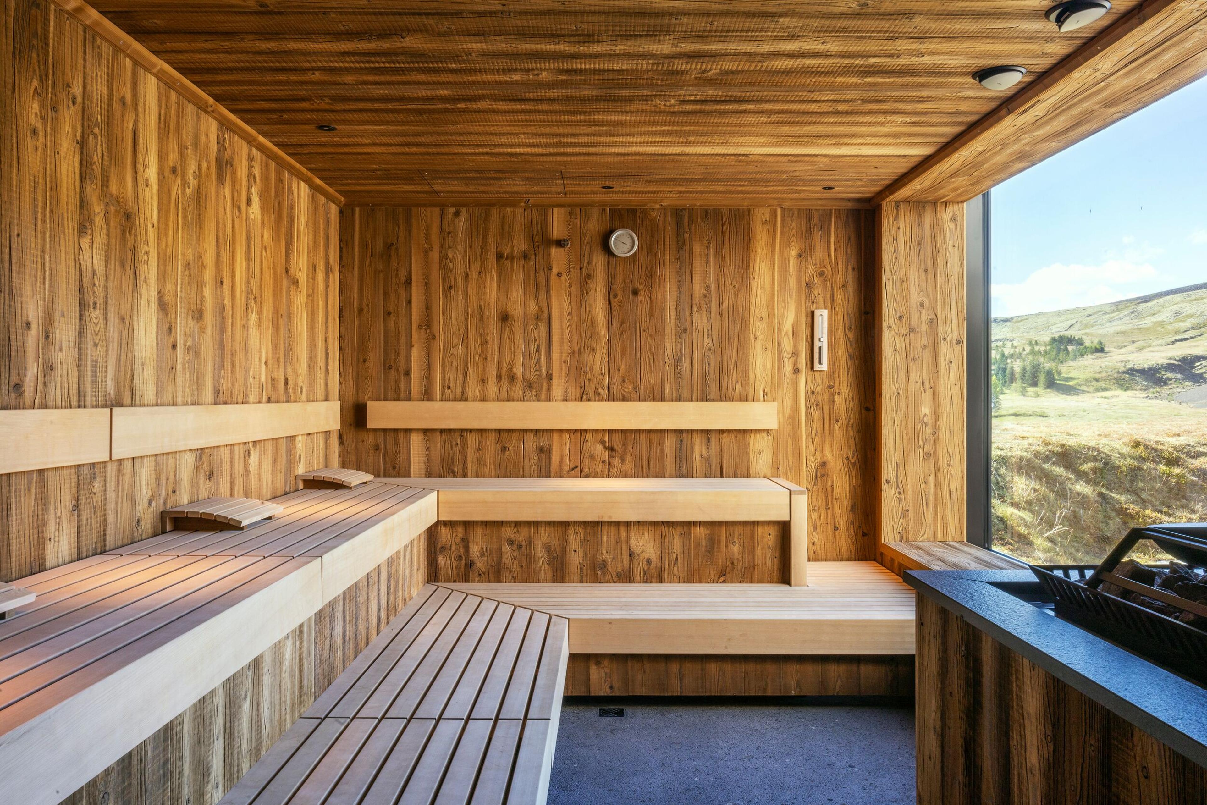 Modern wooden sauna with benches and a large window overlooking a scenic mountain landscape.