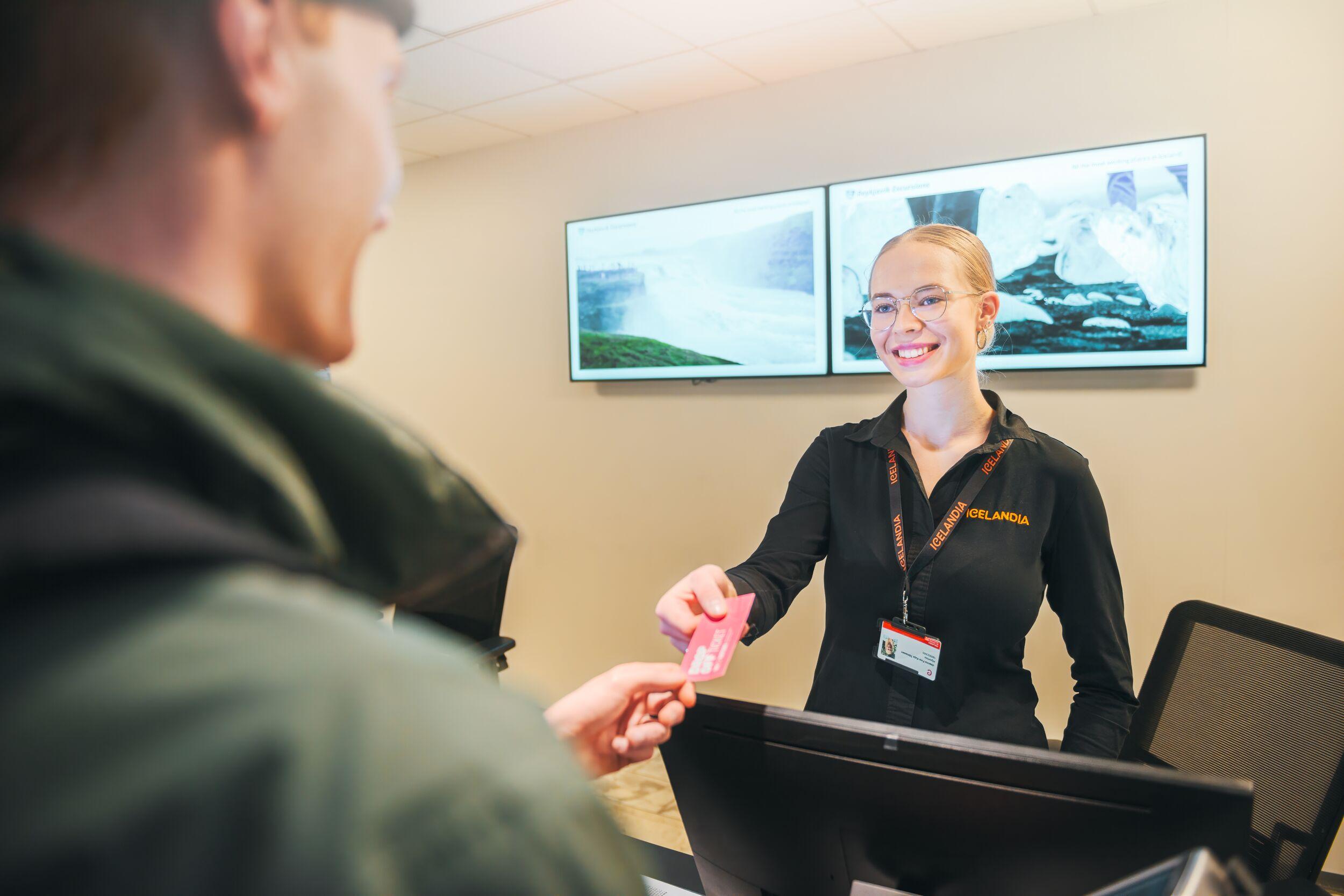A cheerful young customer service representative with a warm smile handing a ticket to a delighted customer.