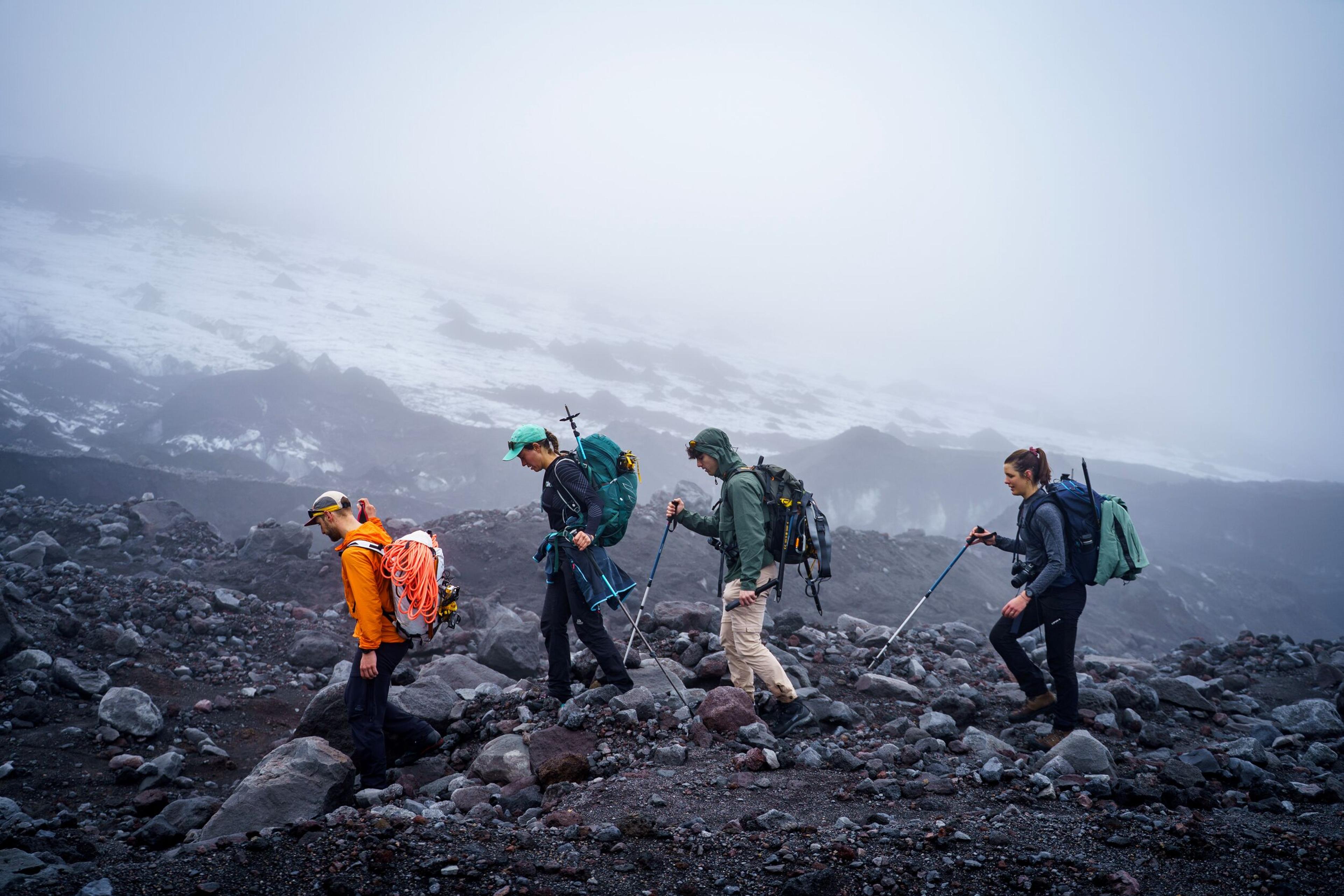 Four hikers with trekking poles and backpacks on a rocky, misty mountain trail.