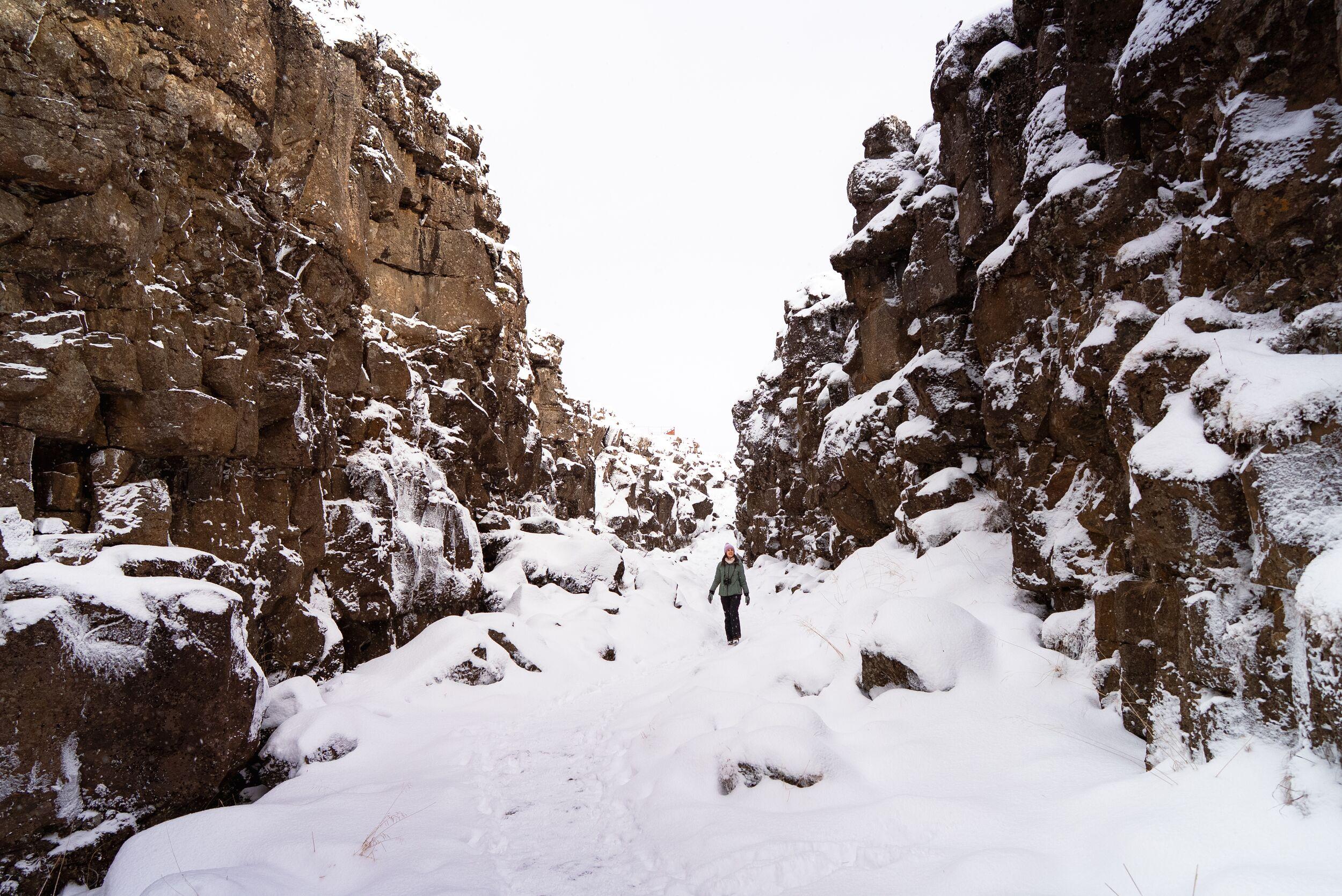 A person walks through a snow-covered rocky canyon.