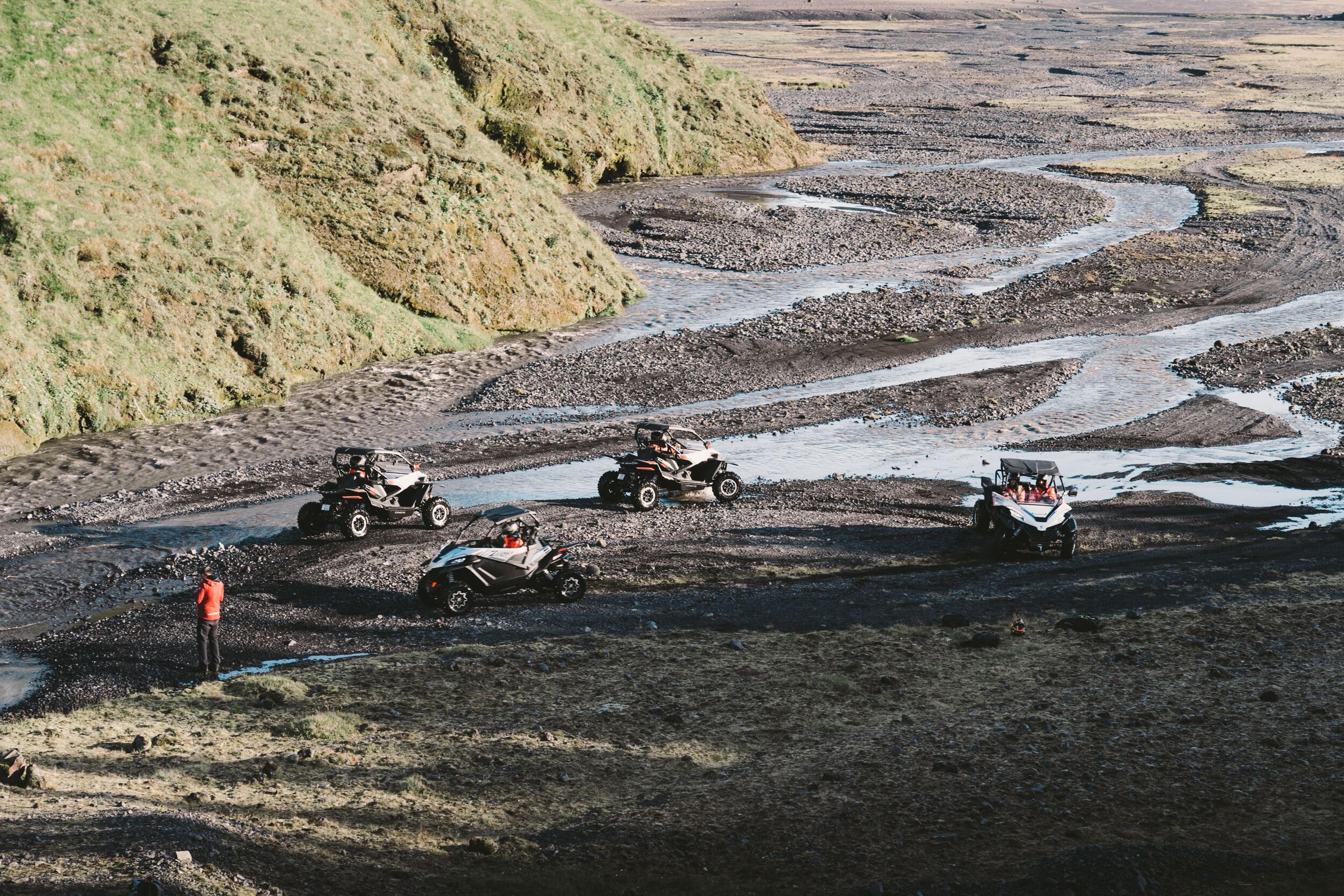 A group of off-road vehicles is navigating through a muddy, winding riverbed