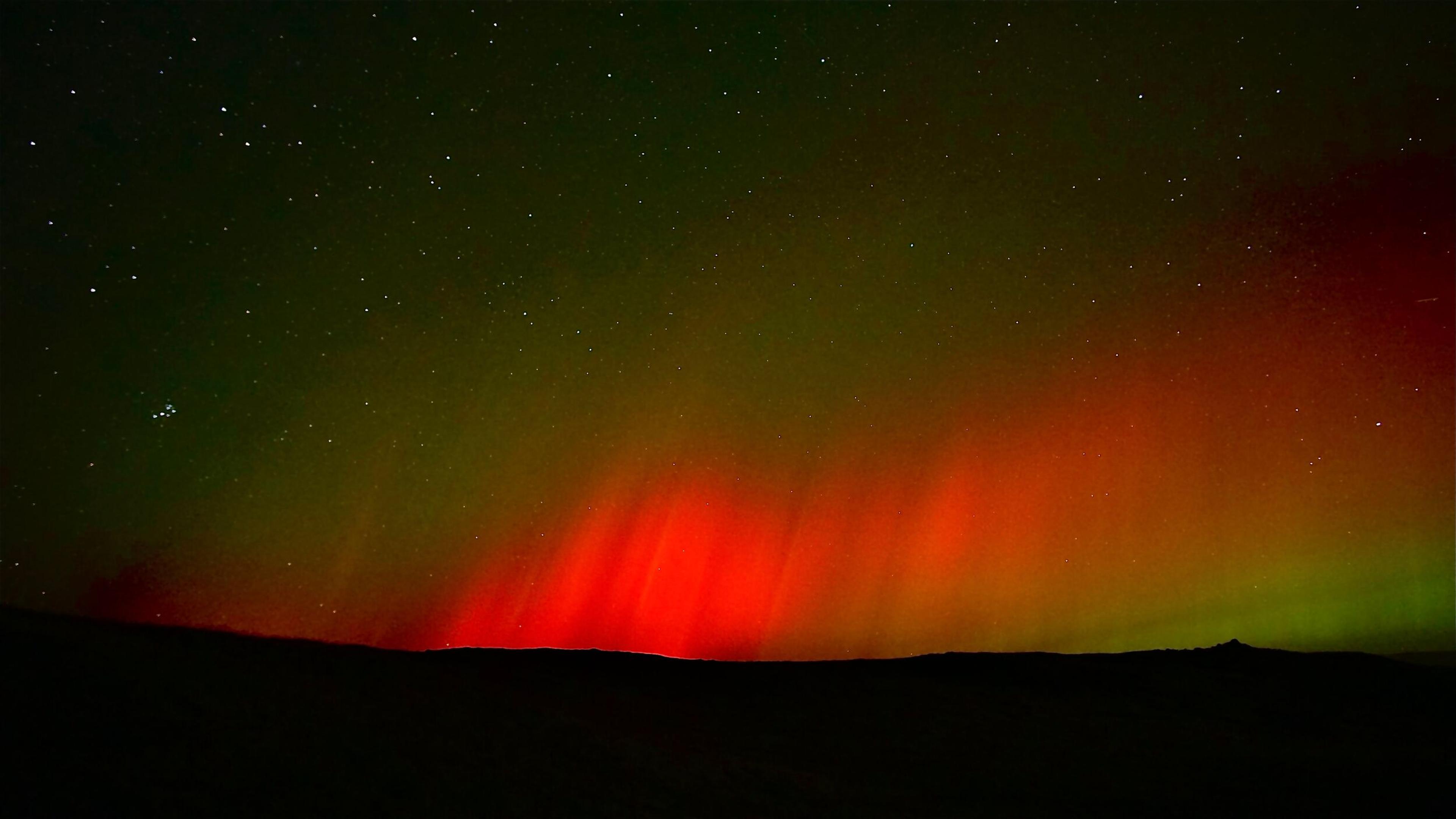 Vibrant red and green aurora in a starry night sky.