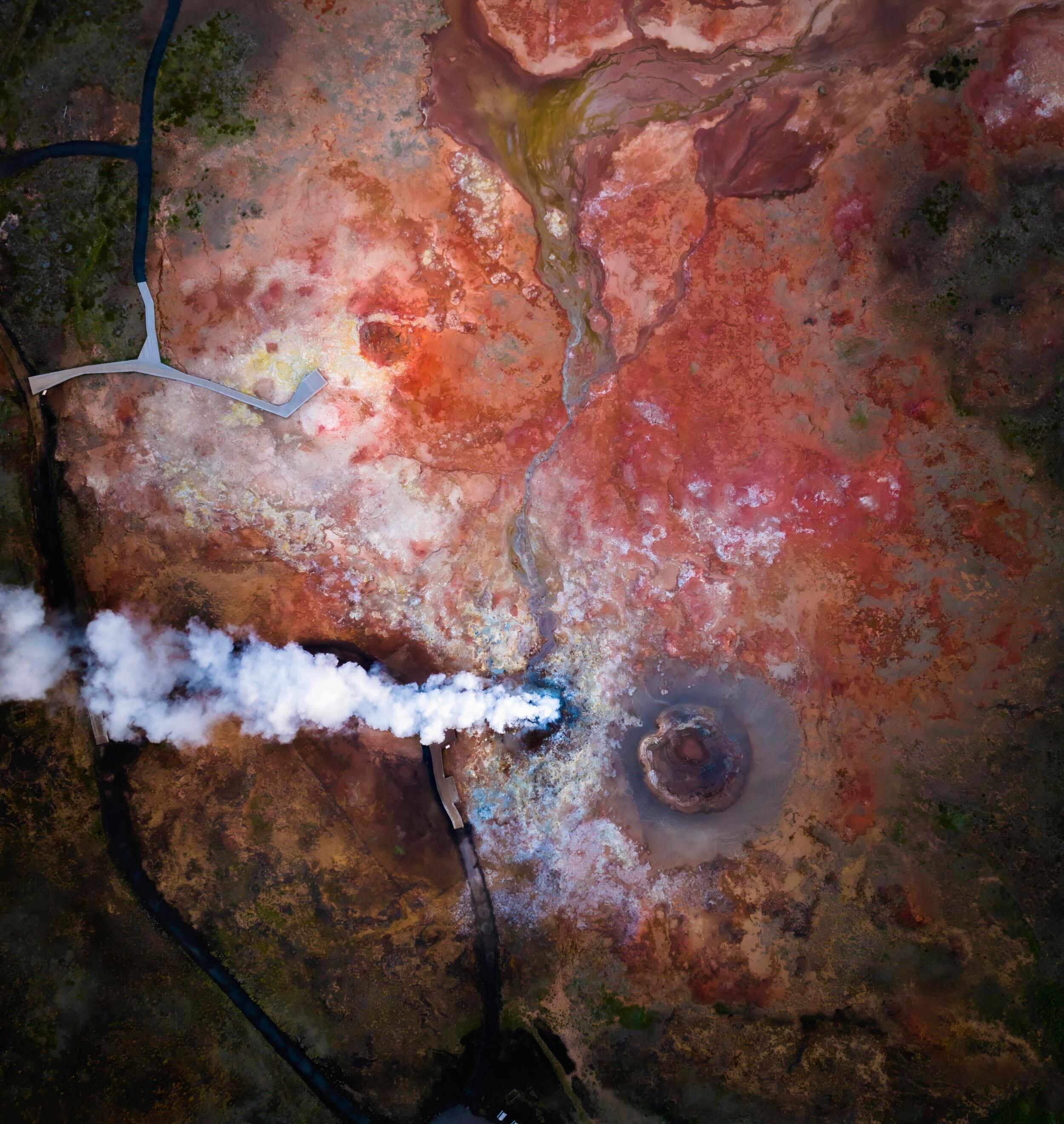 Overhead drone shot of the Reykjanes Peninsula, capturing the vibrant red landscape with plumes of steam rising.