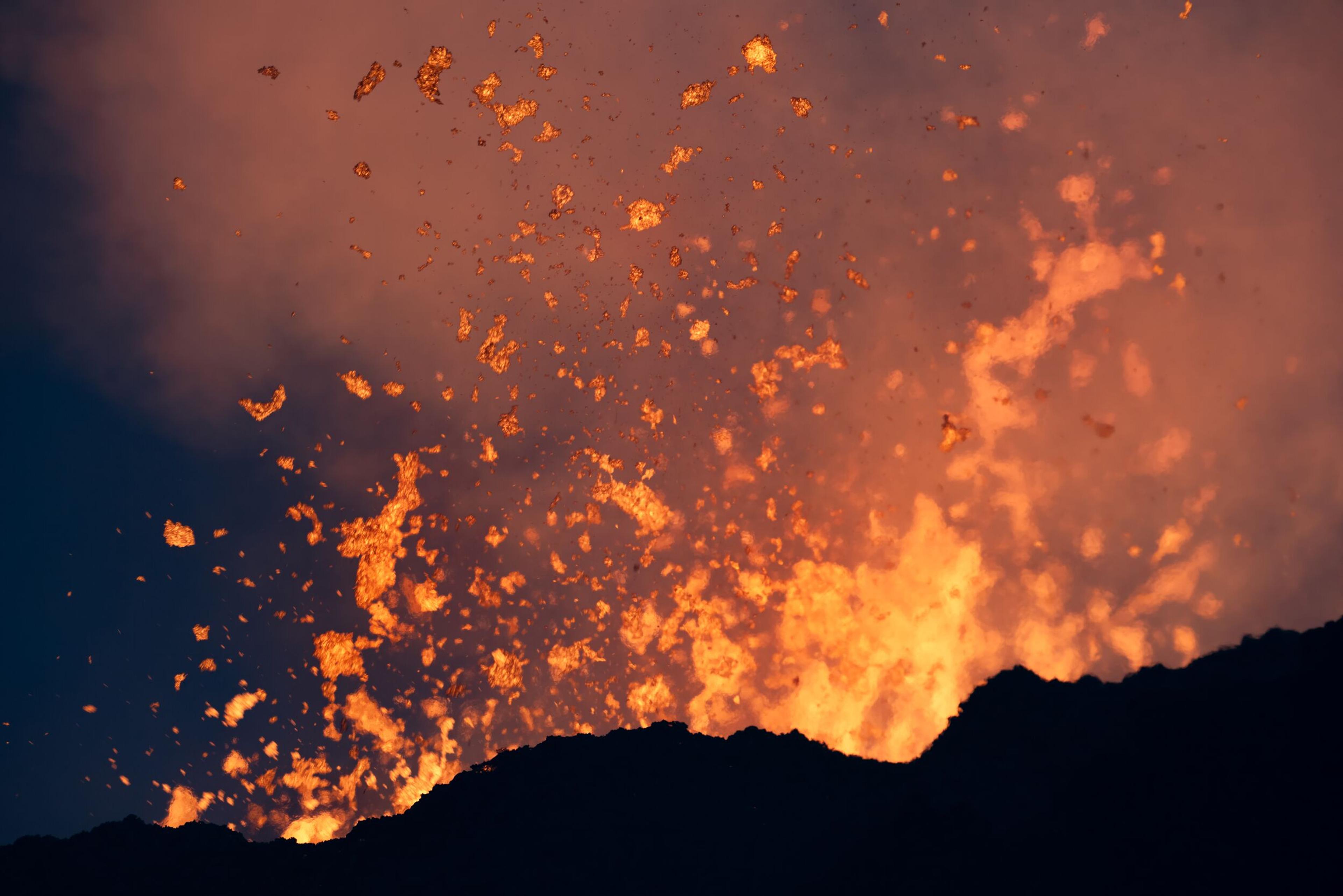 Close-up image of vibrant red lava erupting and splattering into the air, surrounded by billowing smoke.