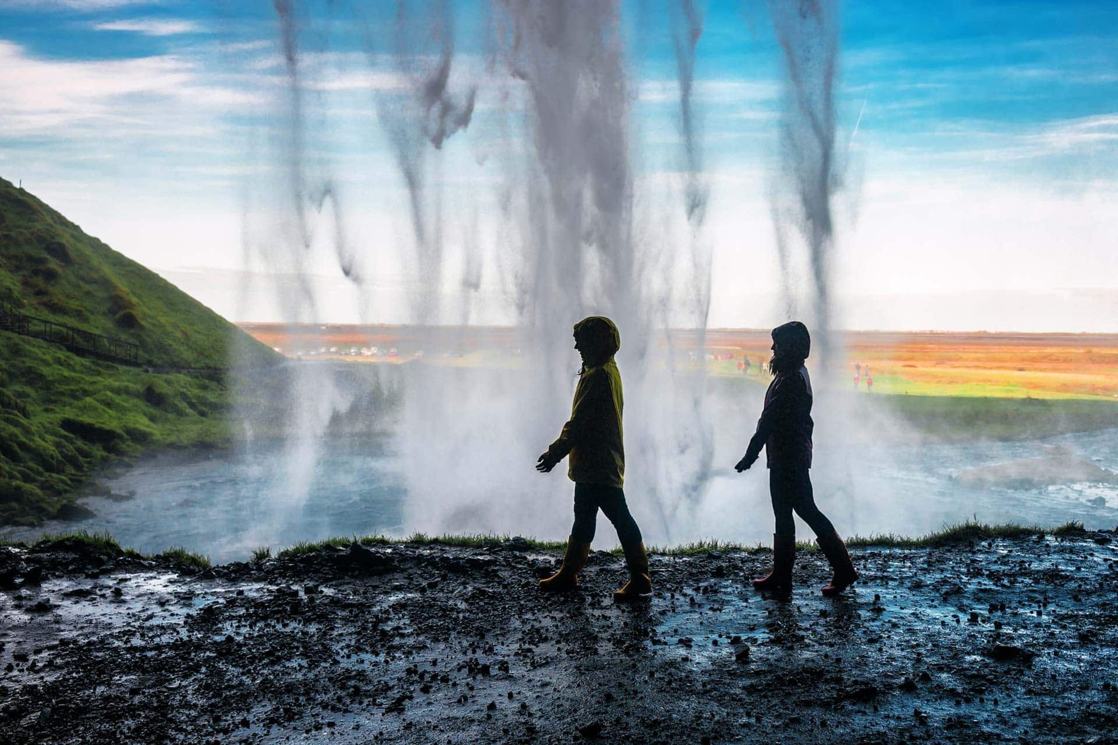 Two children walking behind the Seljalandsfoss waterfall in Iceland, enjoying the unique view and mist.