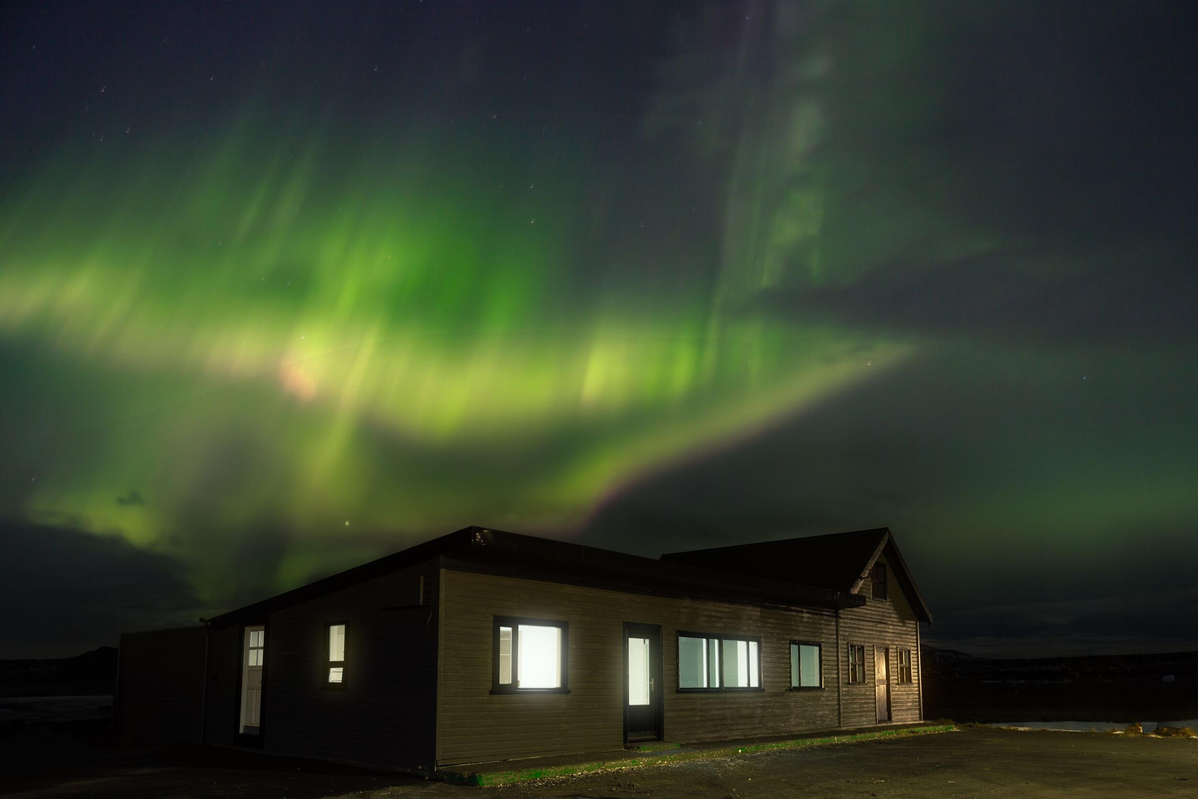 Northern Lights glow green above a dark building with brightly lit windows.