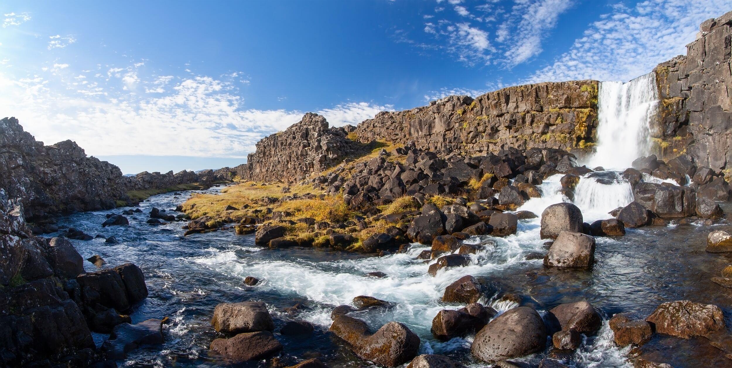Panoramic view of a rocky river flowing through a gorge with a waterfall.