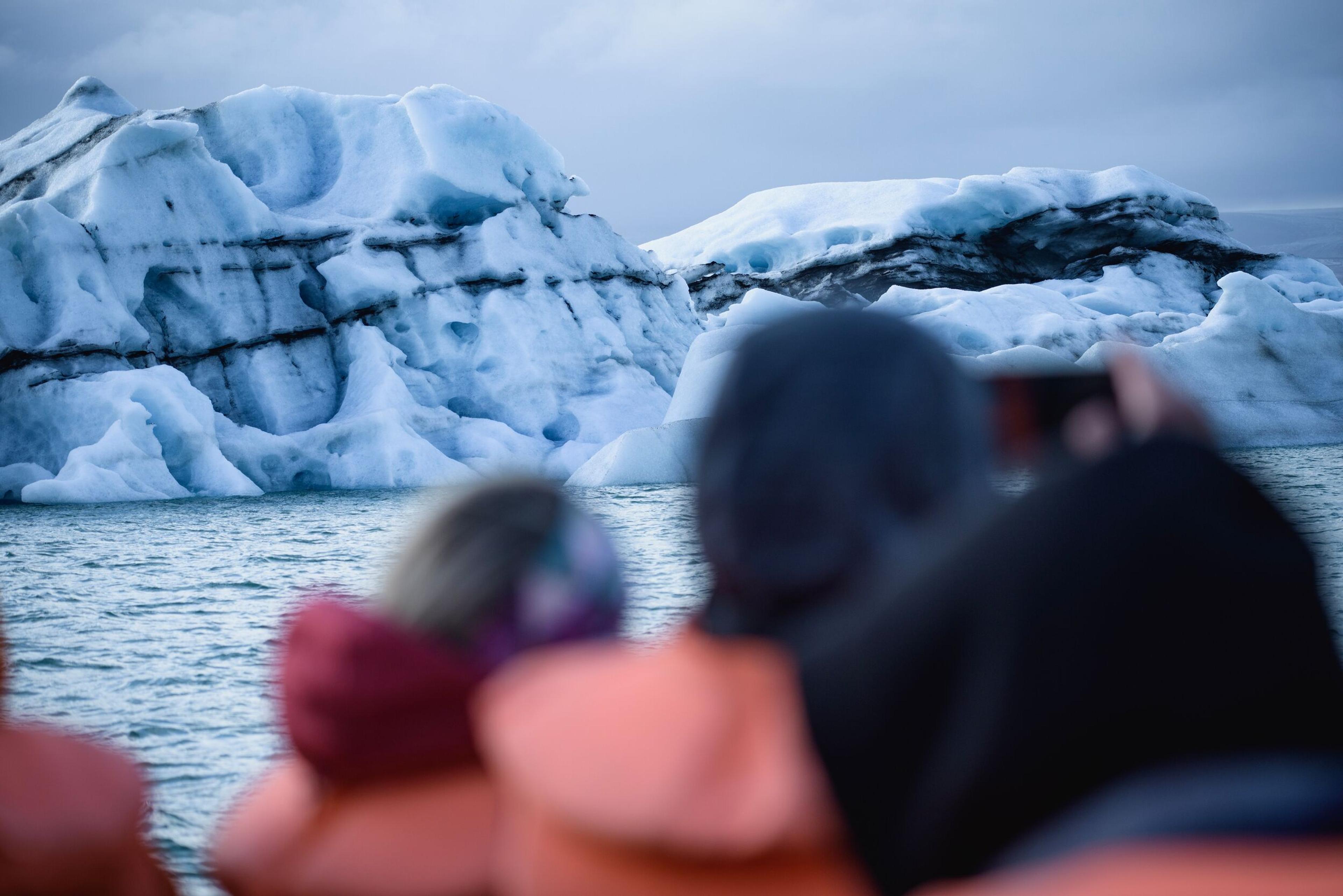 People in life vests on a boat view large icebergs; one takes a photo.