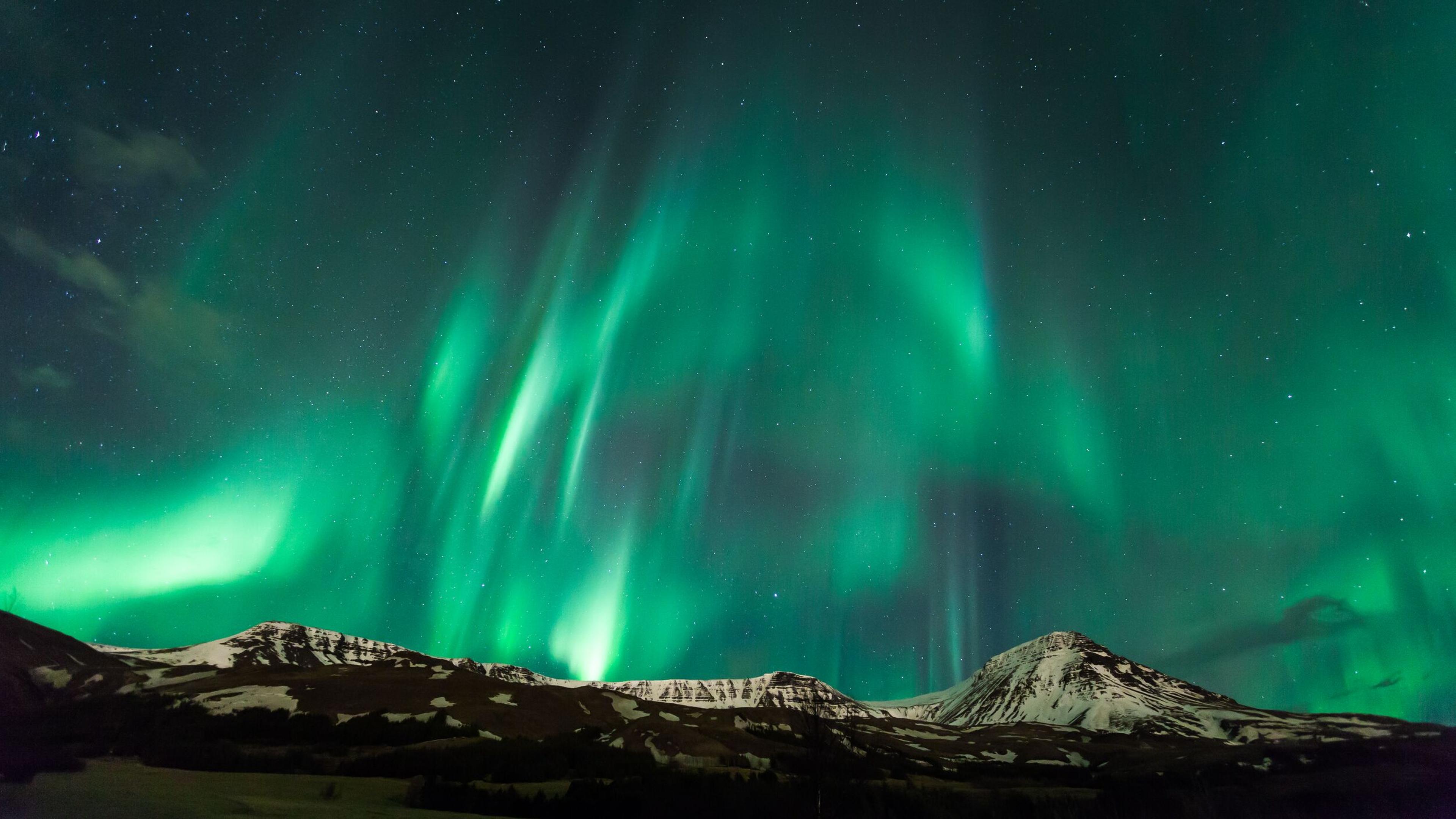 Aurora Borealis streaking over a snow-capped mountain range under a starry sky.