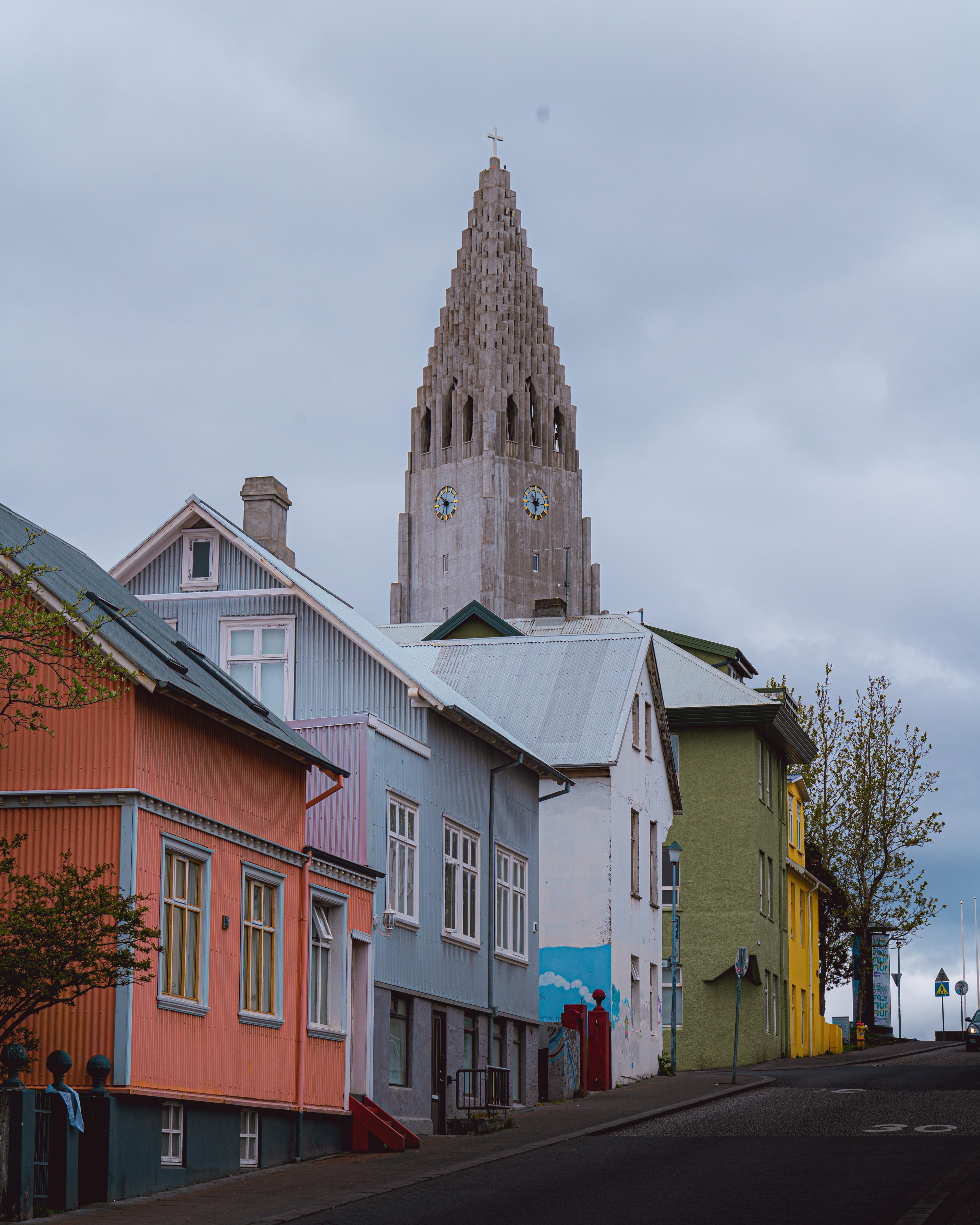 Street view of Reykjavík with the towering spire of Hallgrímskirkja church looming over vibrant-hued houses.