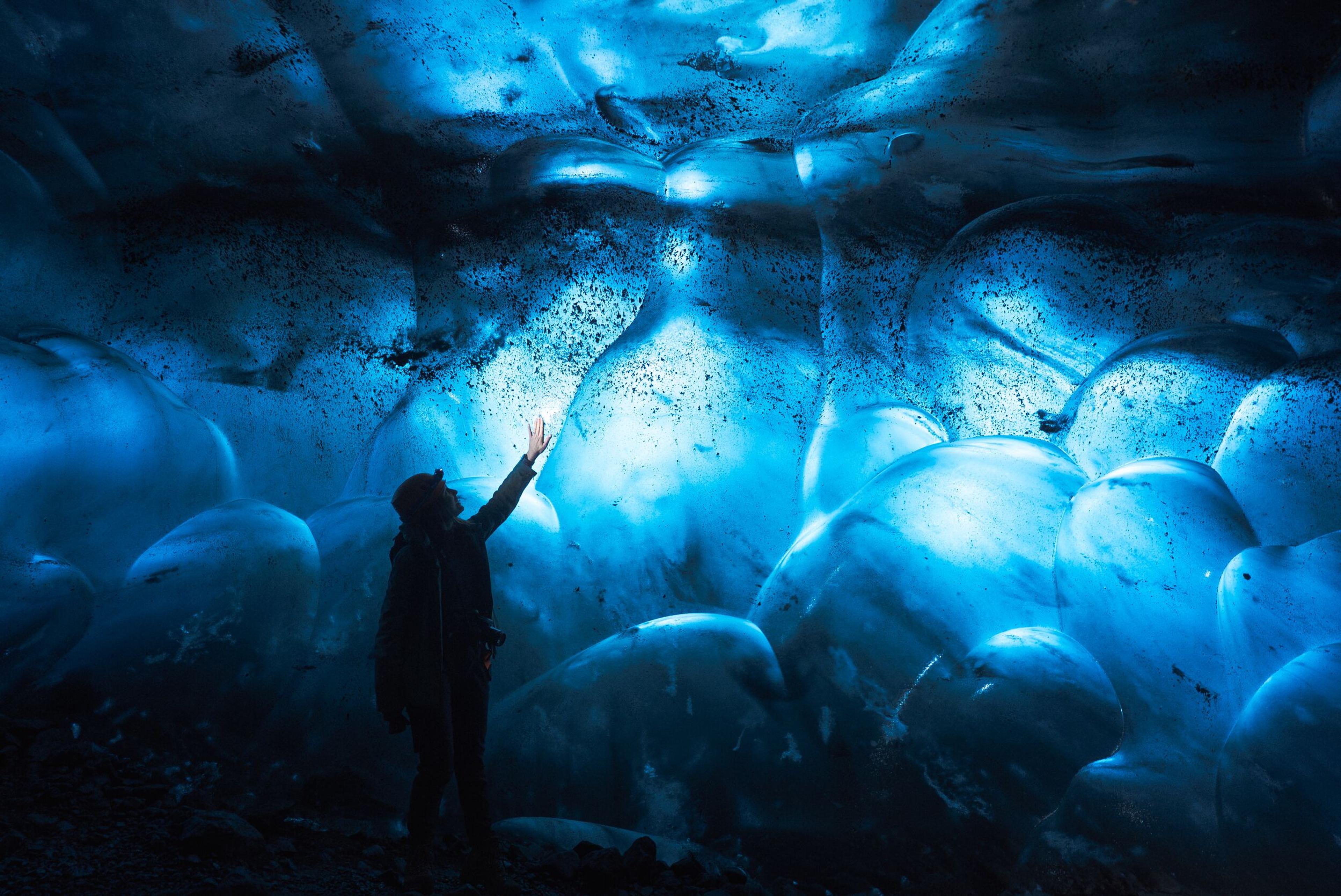 A person touches glowing blue ice inside an ice cave.