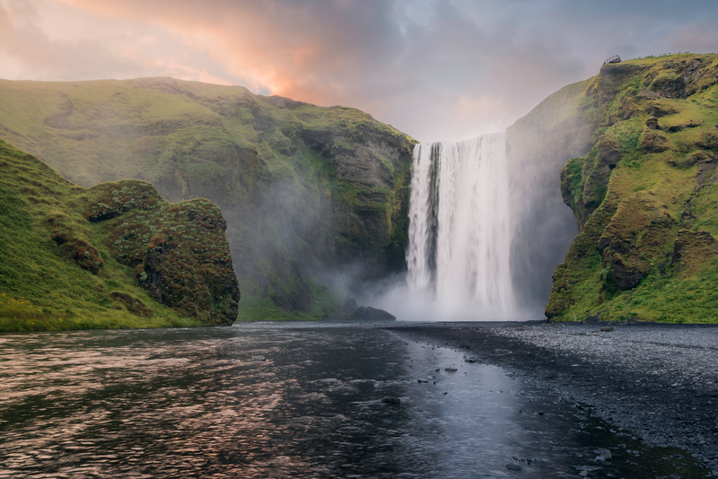 a waterfall in the middle of a river surrounded by mountains