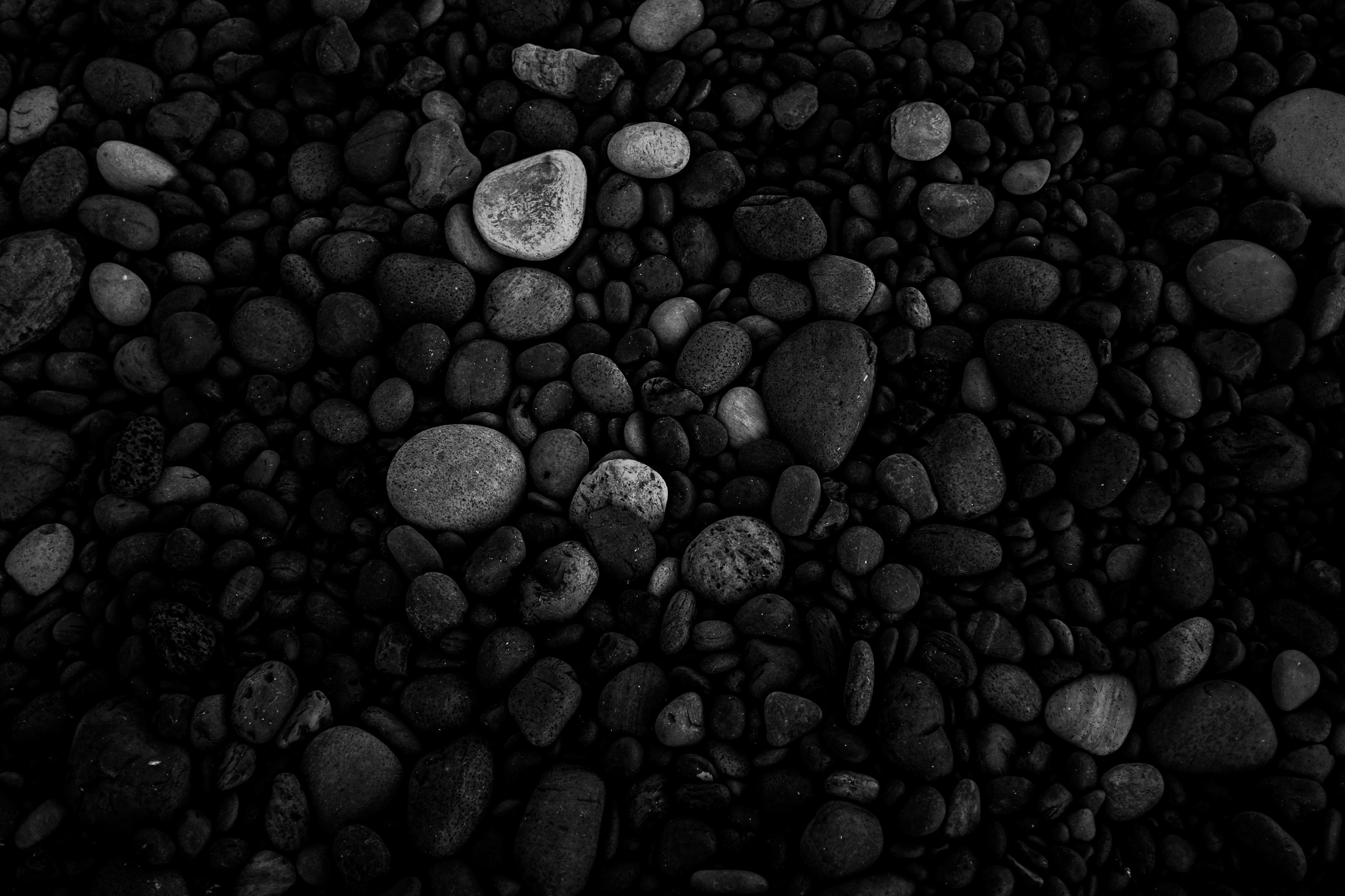 A close-up of smooth black pebbles on a volcanic beach, with a few lighter-colored stones creating contrast in the dark, textured landscape.