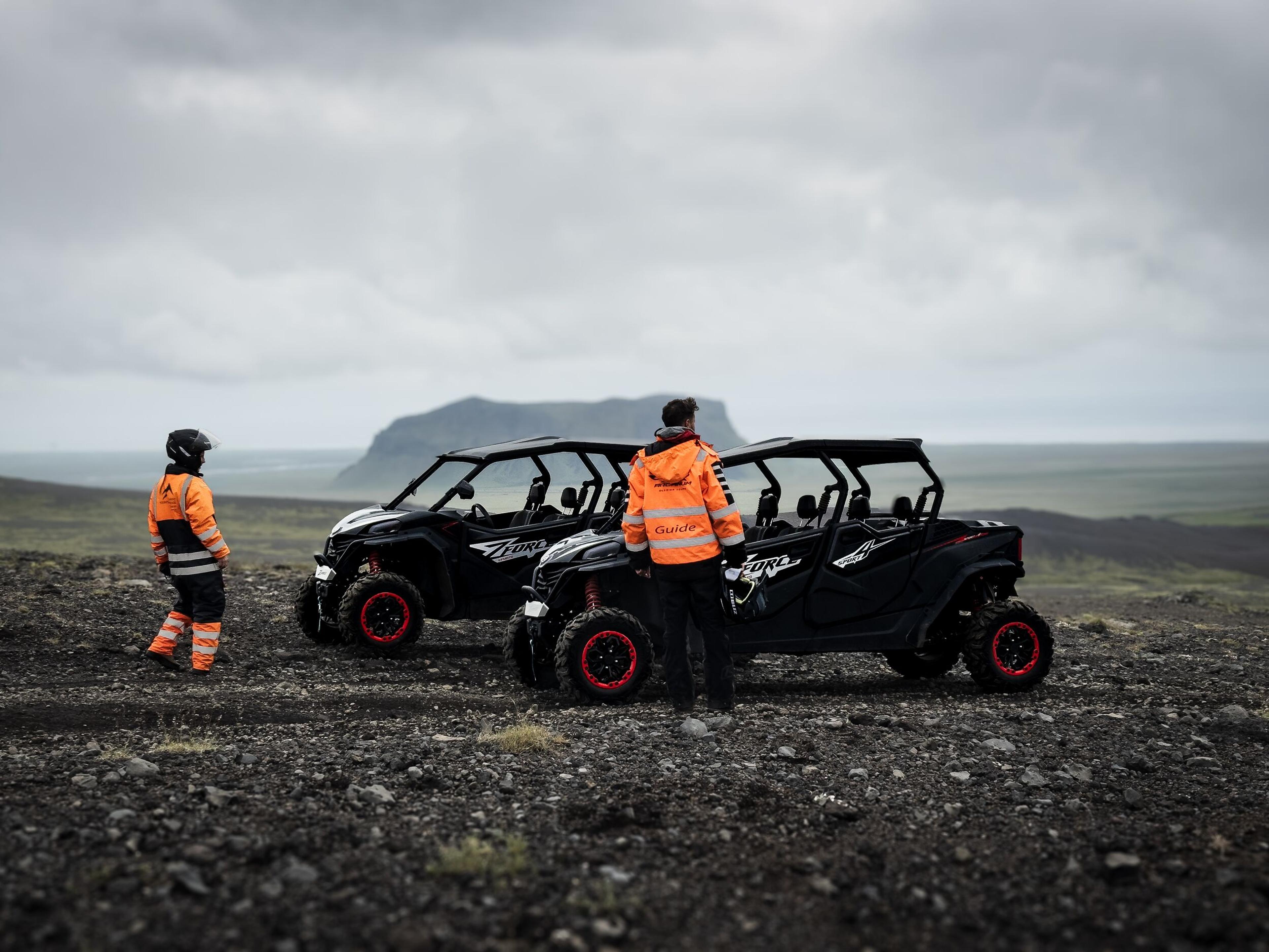 Two off-road buggies with red-rimmed tires on the South Coast of Iceland, with drivers in orange jackets and helmets.