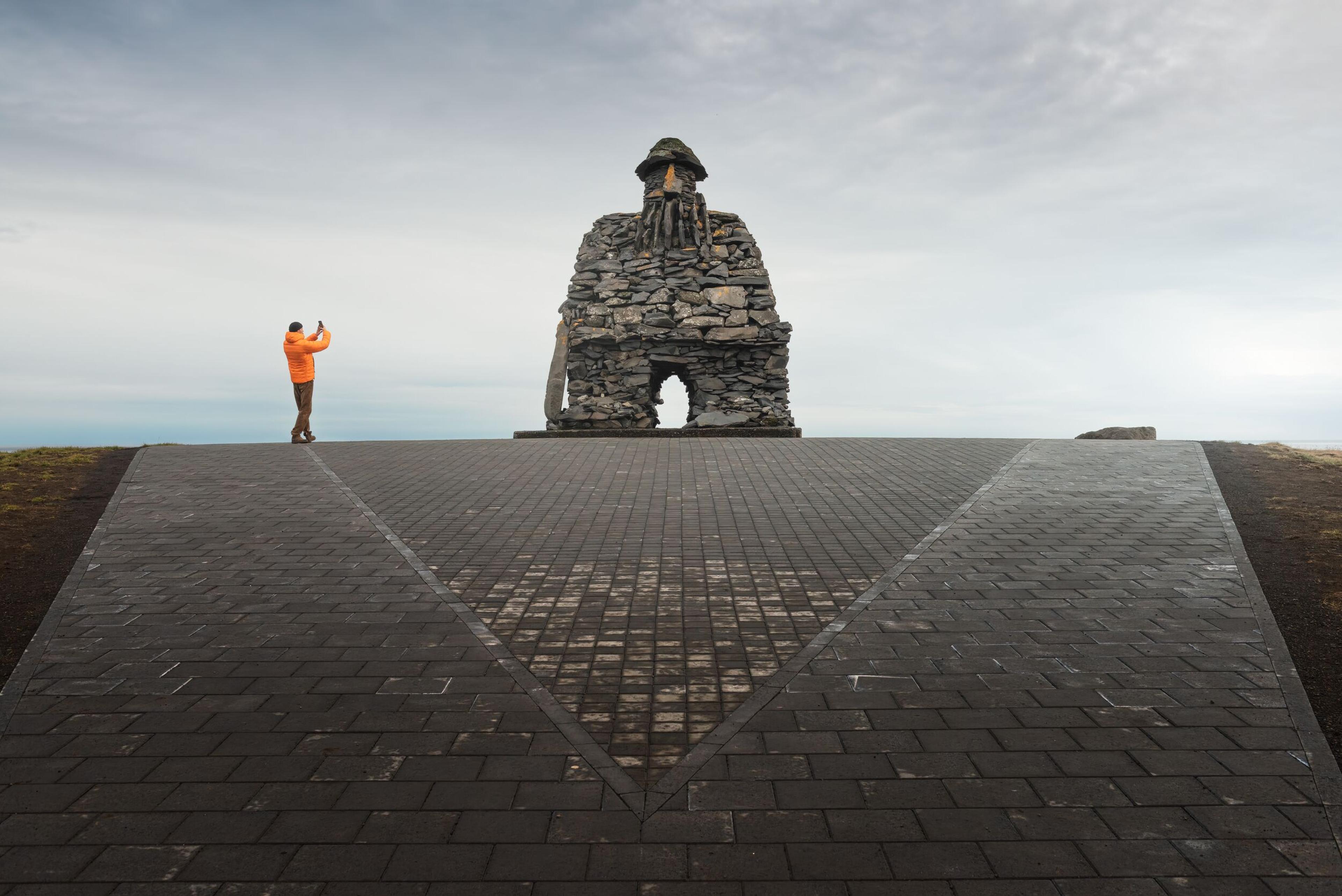 An explorer taking a picture of a statue in Arnarstapi, Iceland